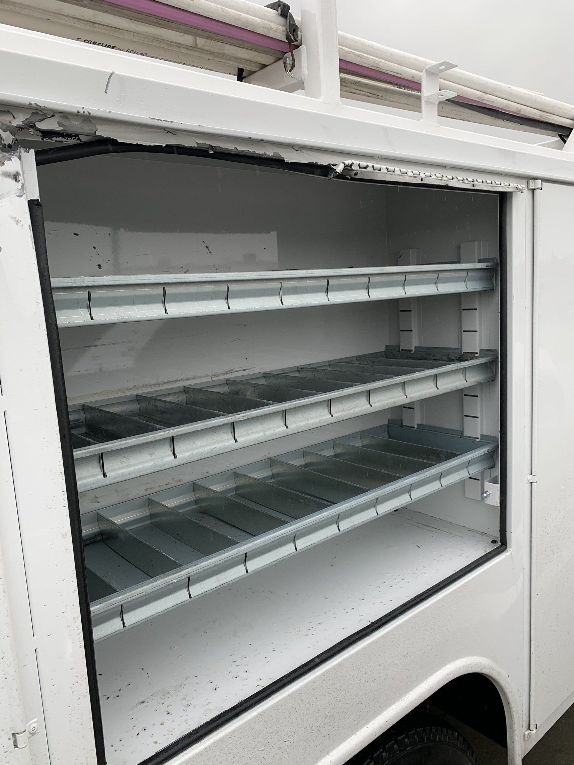 White utility truck side storage with three metal shelves.
