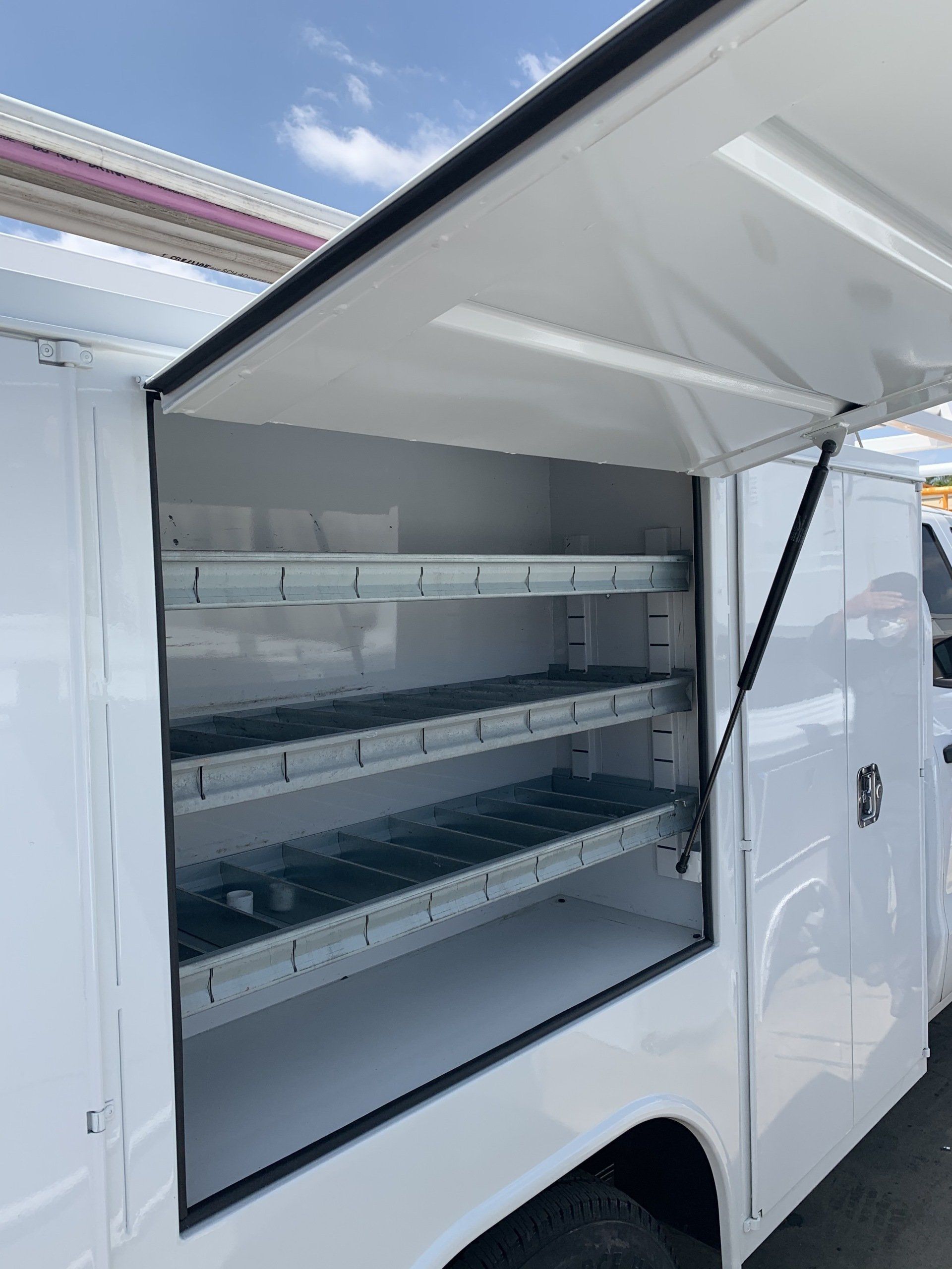 White service truck storage compartment with open door, three shelves.