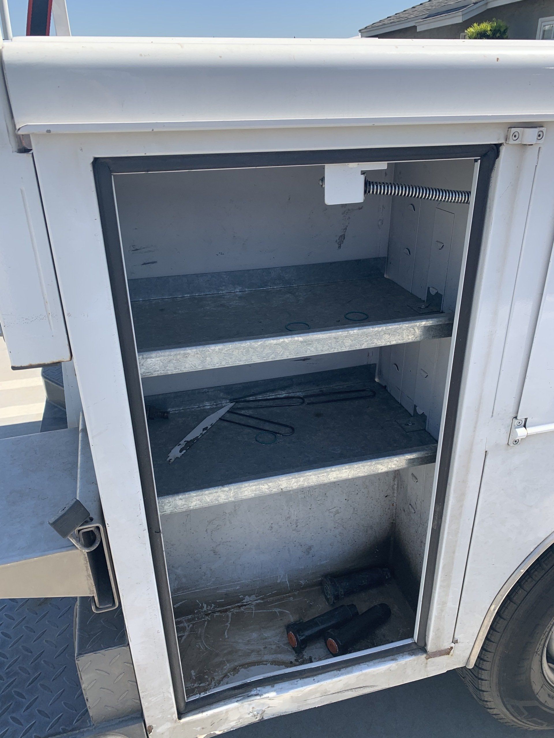 Open white storage compartment with metal shelves on a truck.