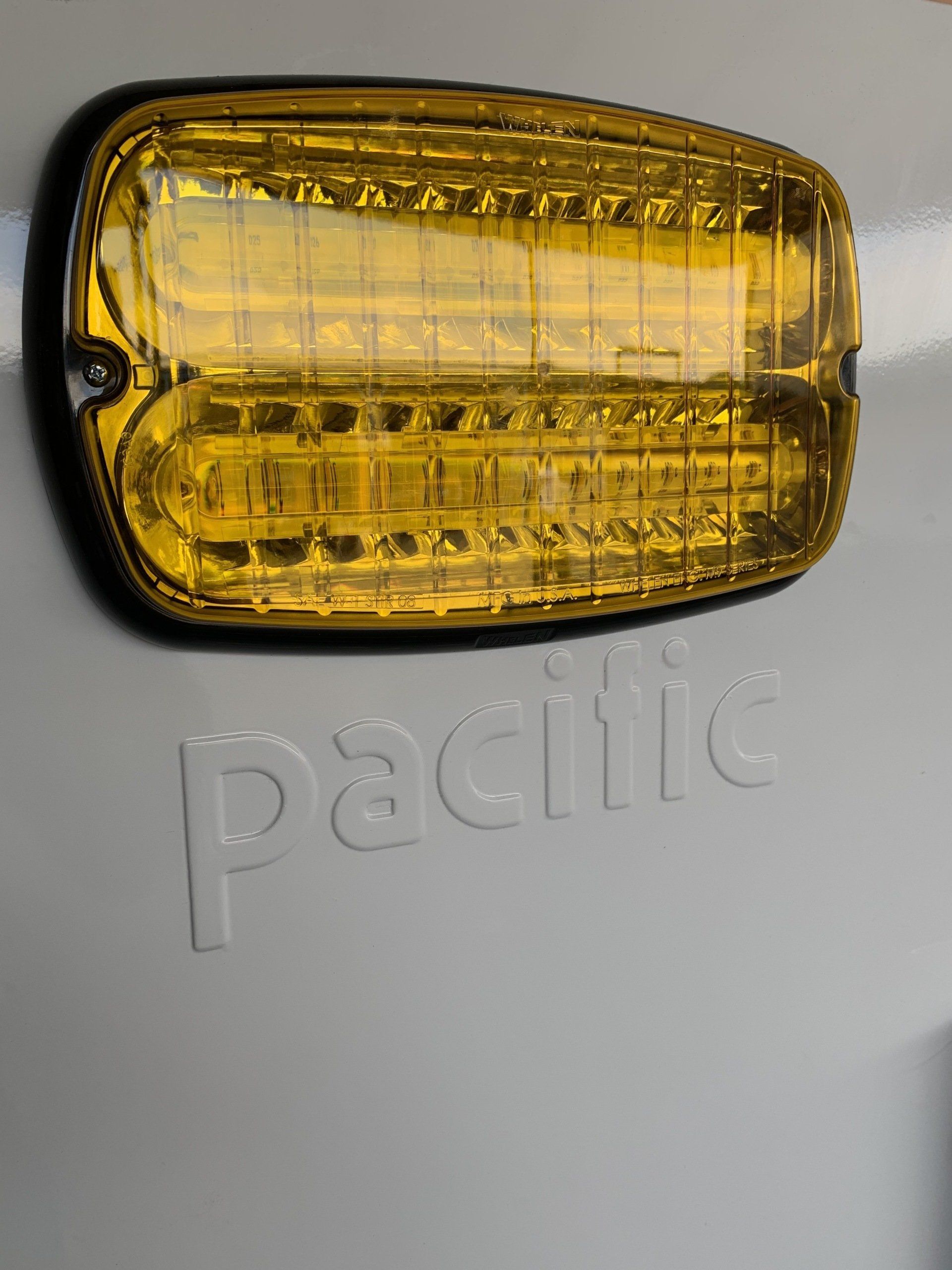 Yellow light fixture mounted on a gray surface with the word