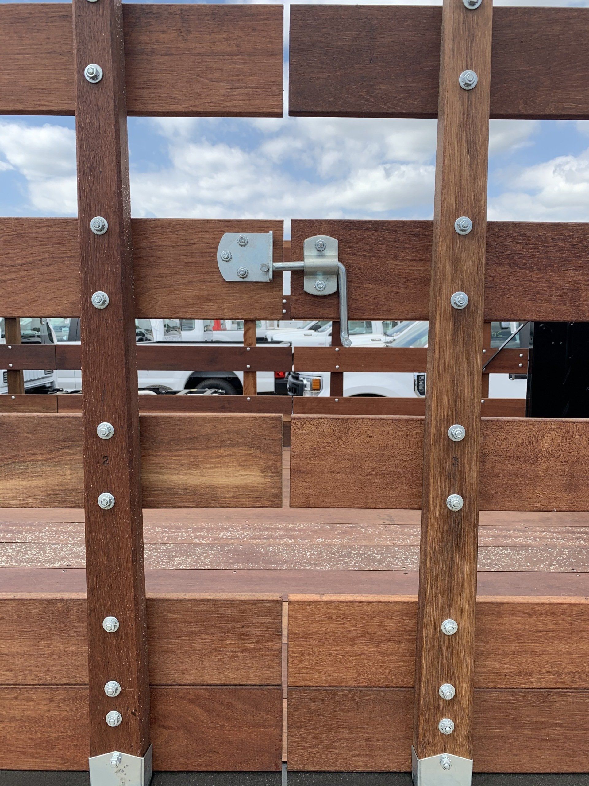 Wooden gate with metal hardware. Brown wood planks, blue sky visible, bolted supports.