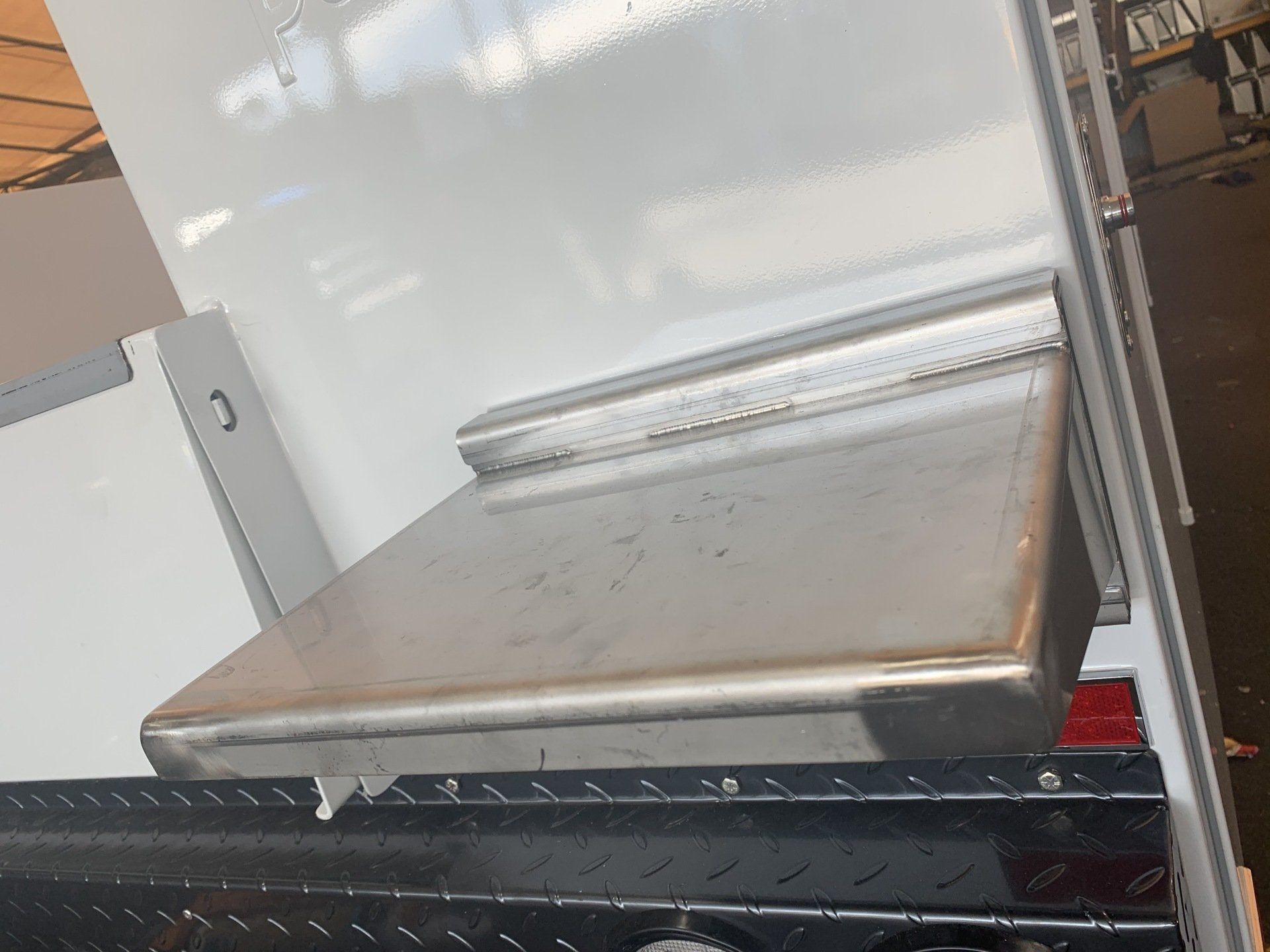 A silver toolbox mounted on a white surface, with a black diamond-plate area below.