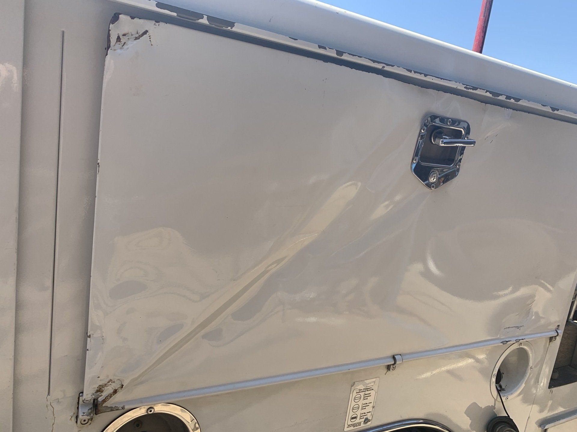 Cream-colored vehicle panel with dents, a latch, and other hardware.
