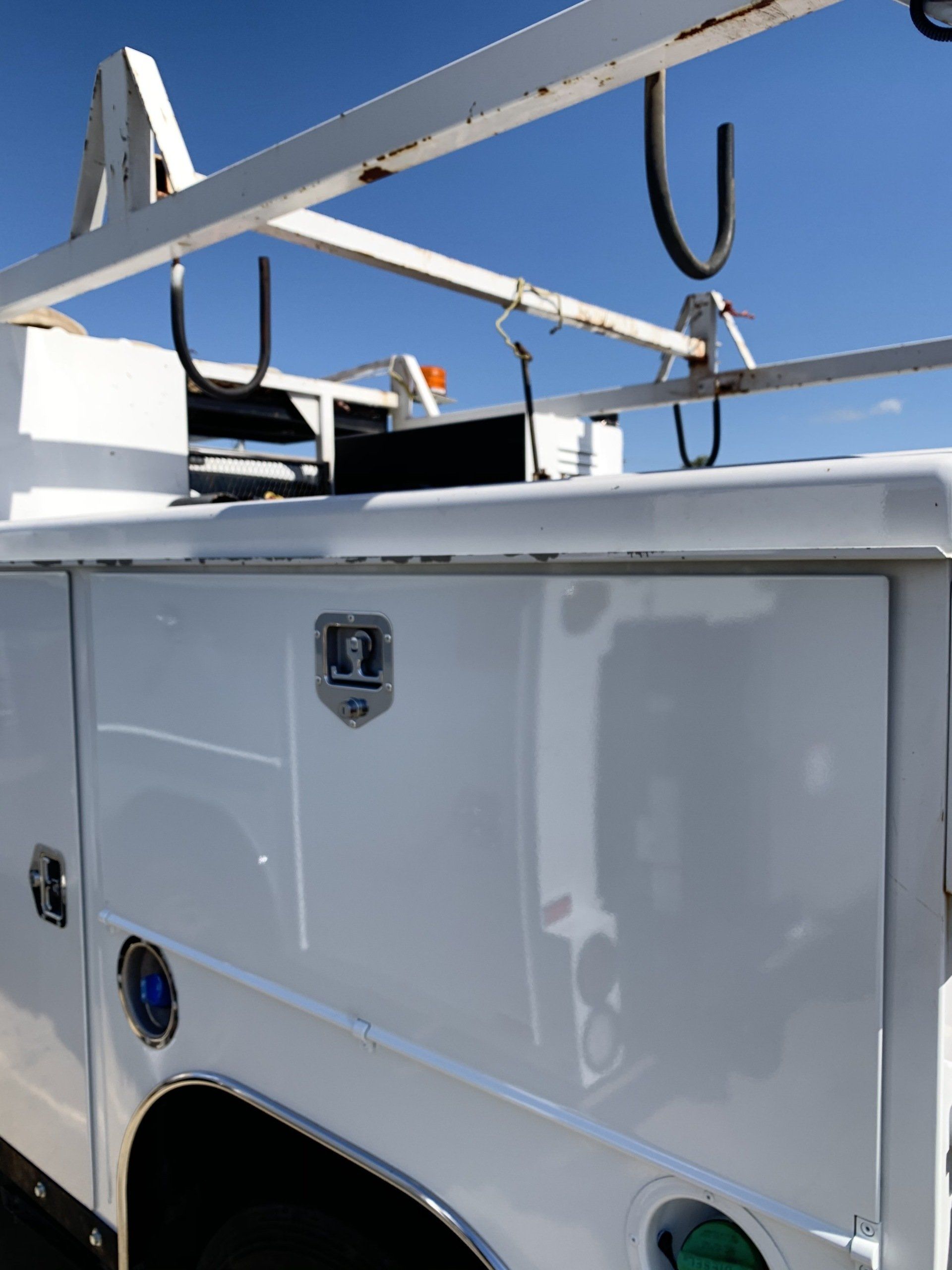 White utility truck with ladder rack and side storage compartments against a blue sky.