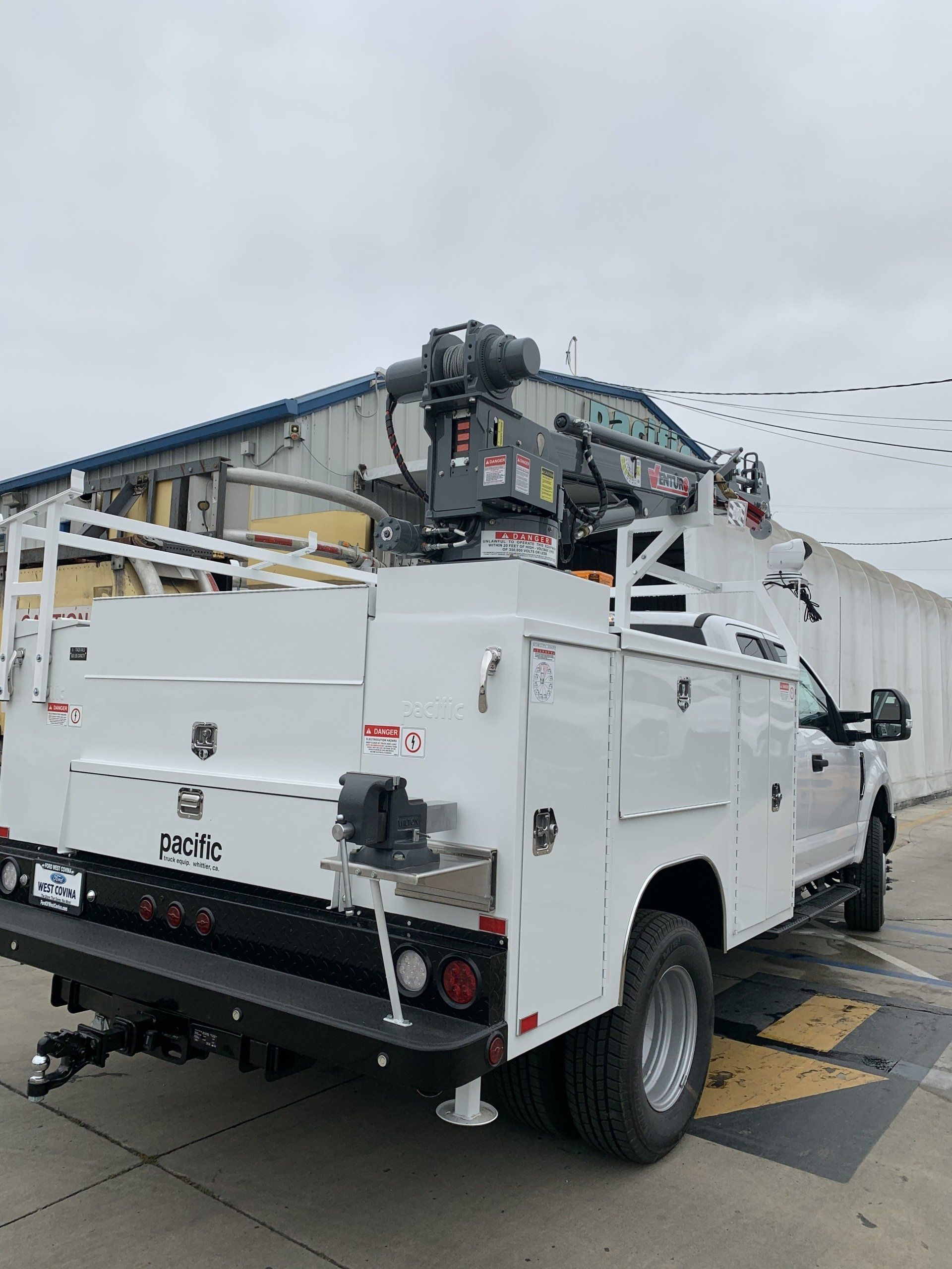 White work truck with a crane attachment parked in front of a building.