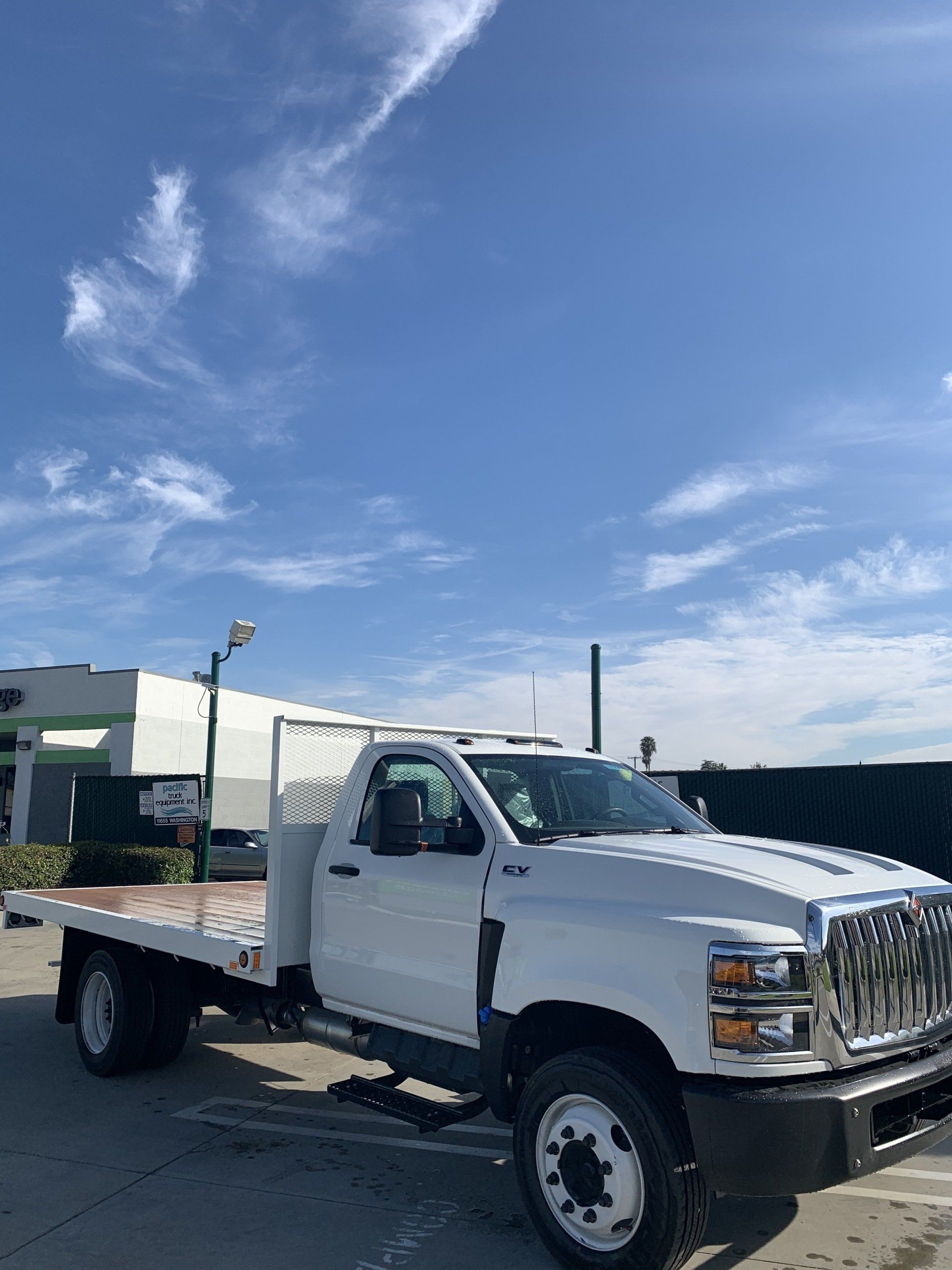 White flatbed truck parked under a blue sky with scattered clouds.