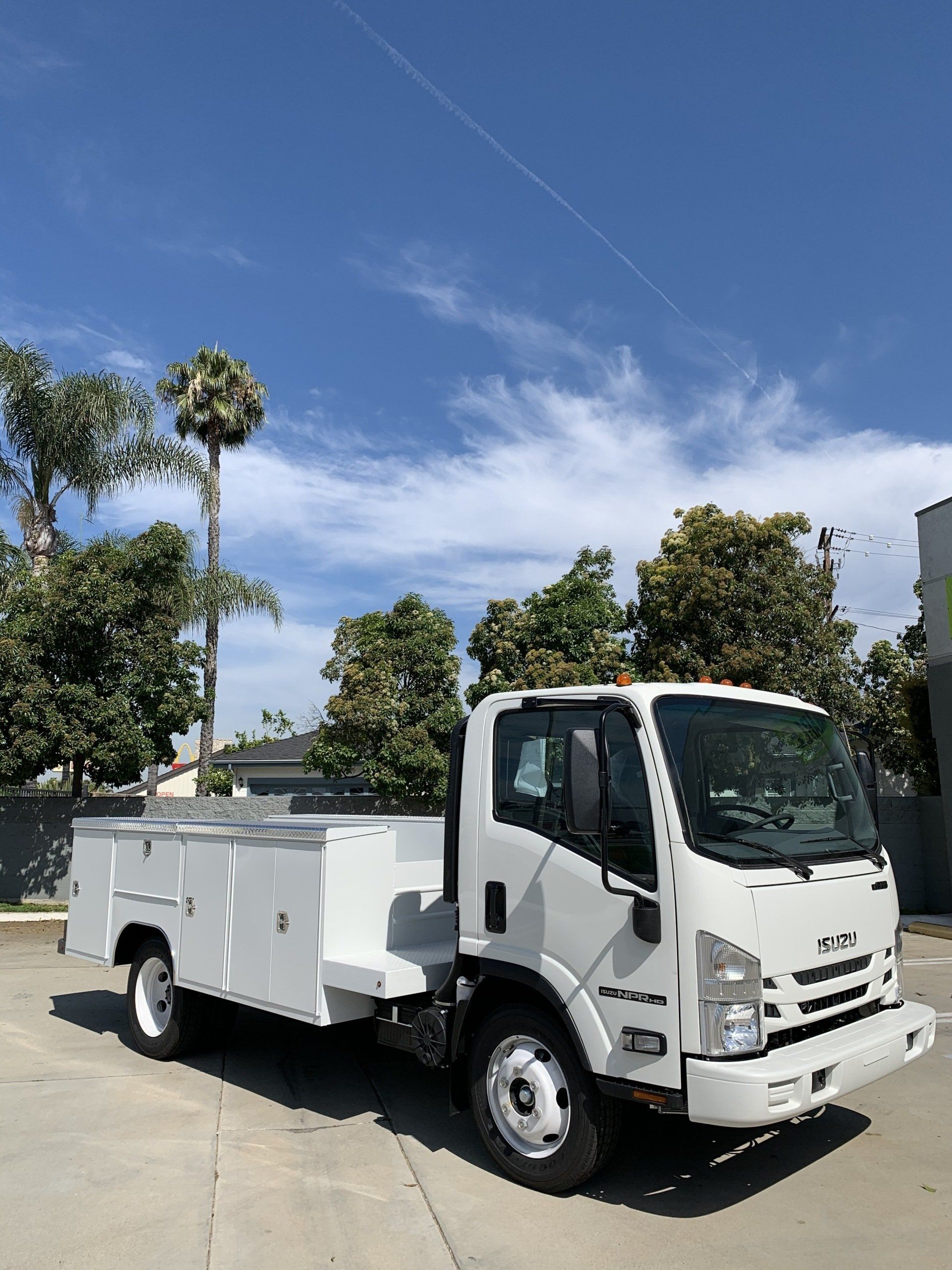 White work truck parked on a paved lot with trees and blue sky.