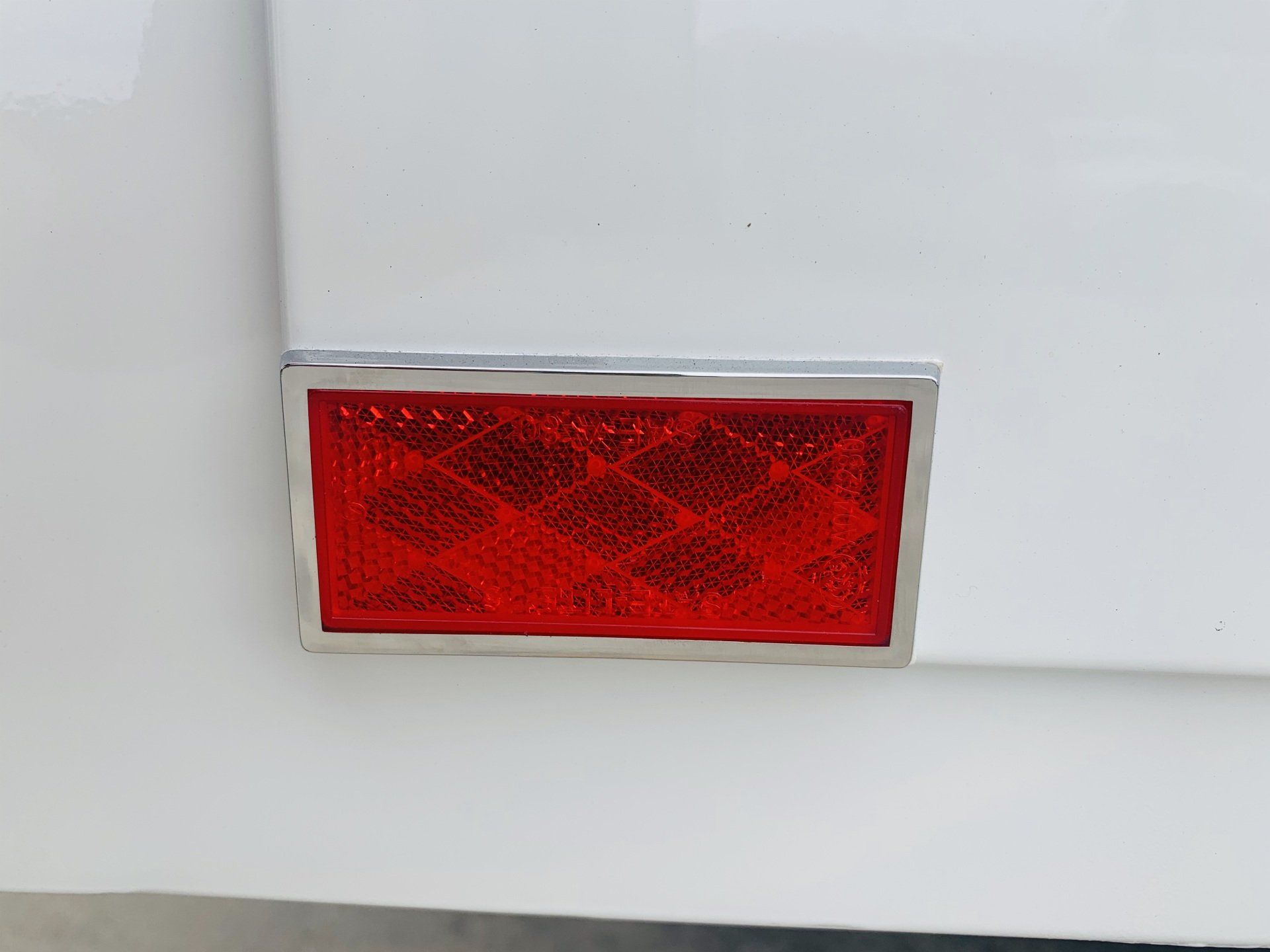 Red rectangular reflector with a chrome frame on a white surface.