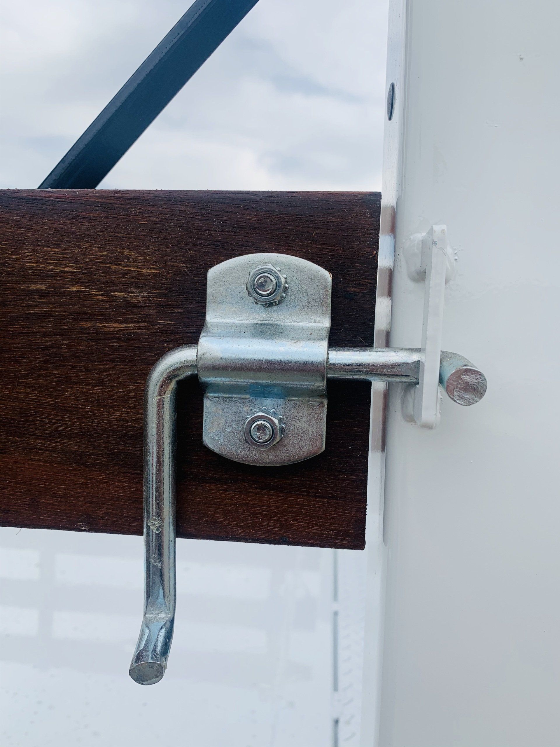 Metal latch securing a brown wooden beam to a white metal frame.