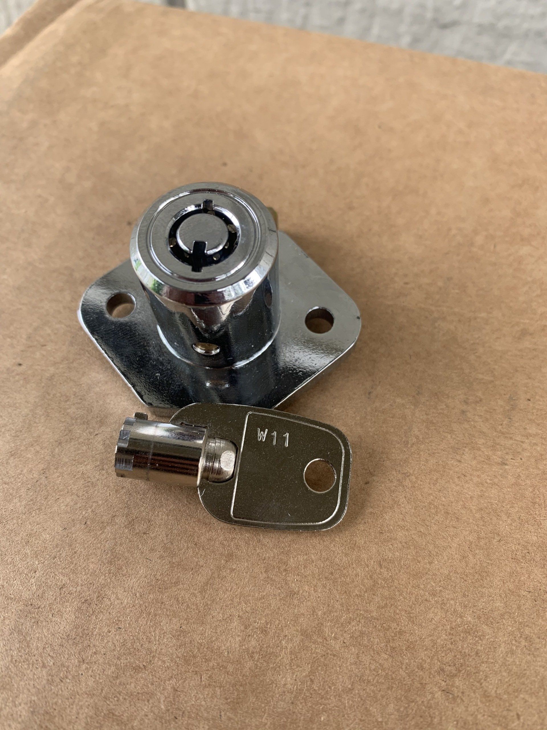 Chrome cabinet lock with key on a brown surface.