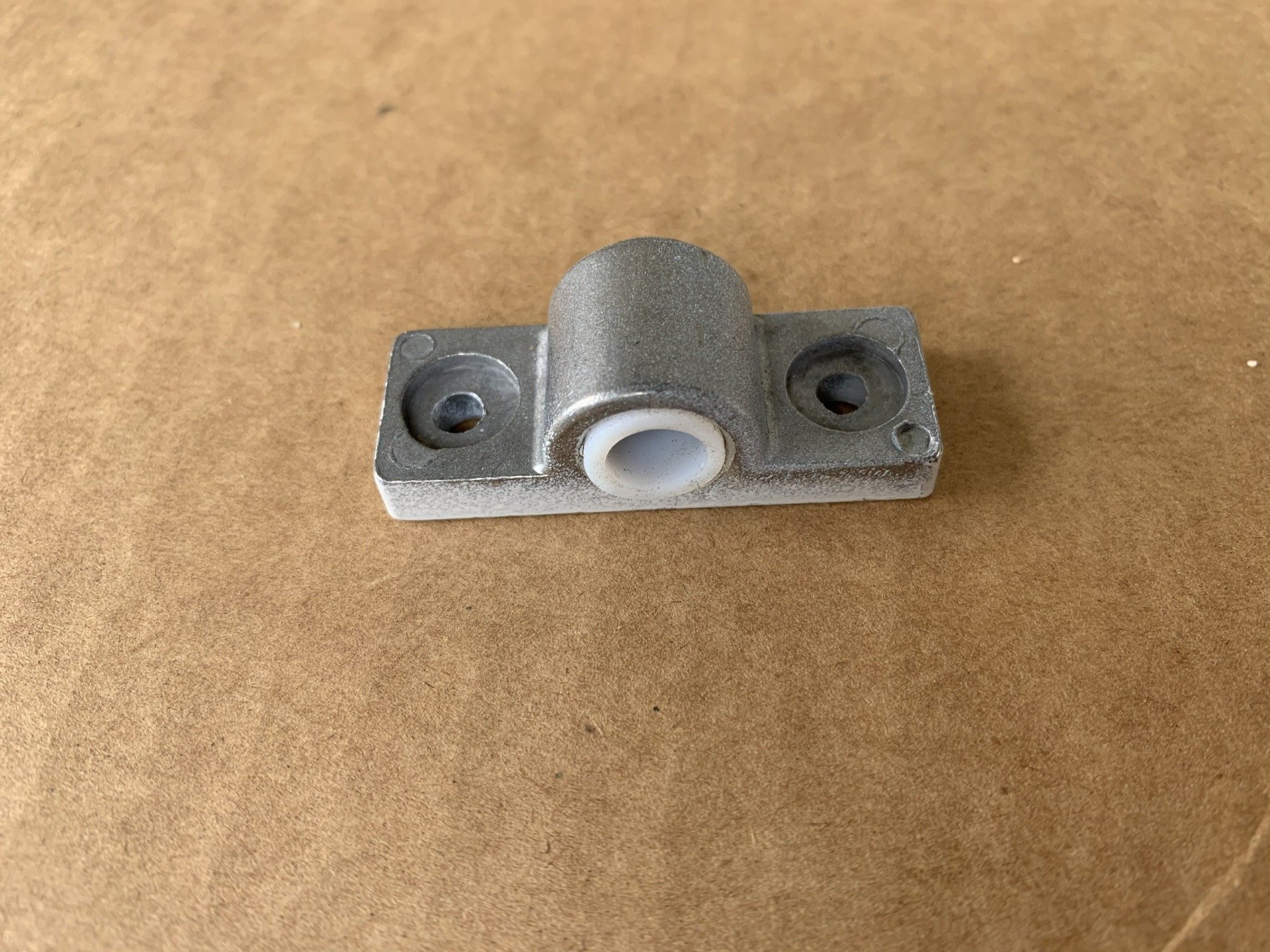 Gray metal doorstop with a white plastic insert, two screw holes, on a brown surface.