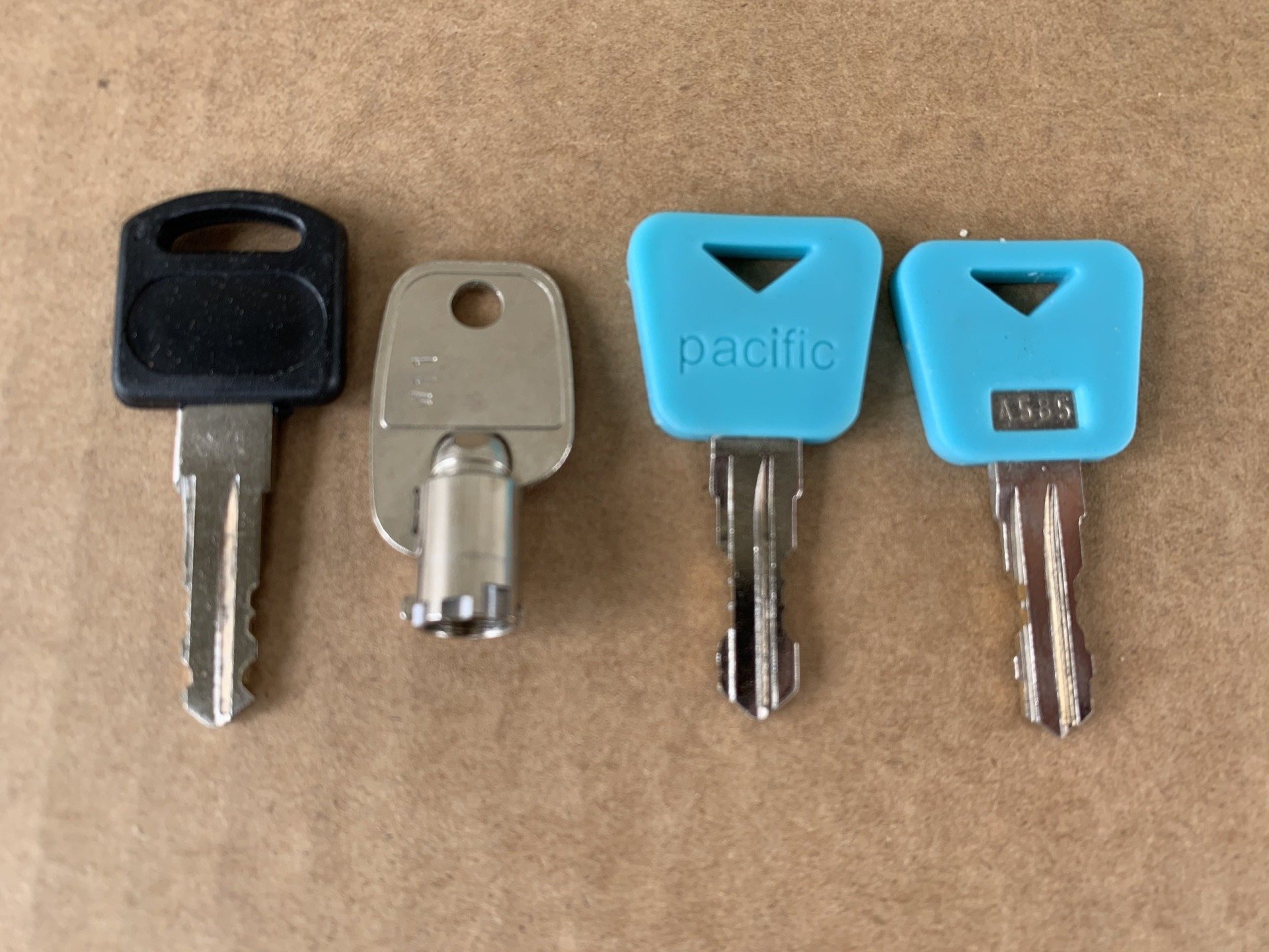 Four metal keys of different shapes and handle colors on a brown surface.