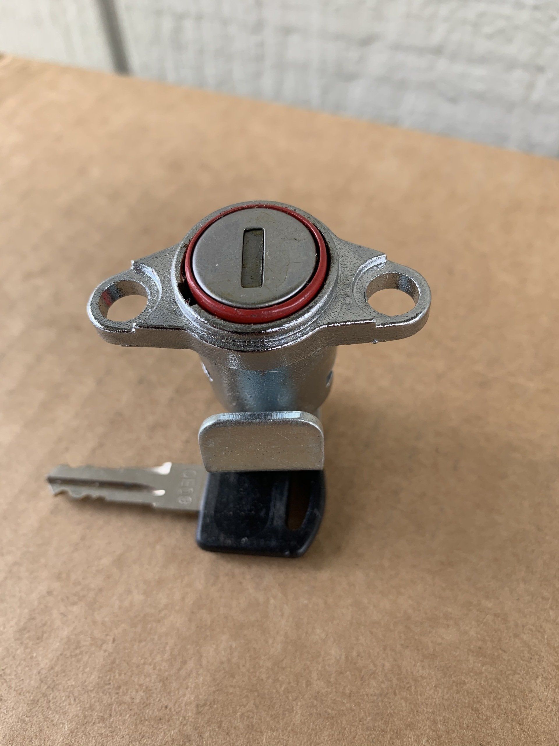Close-up of a silver keyed lock with key inserted, black base, and a red gasket on a brown surface.