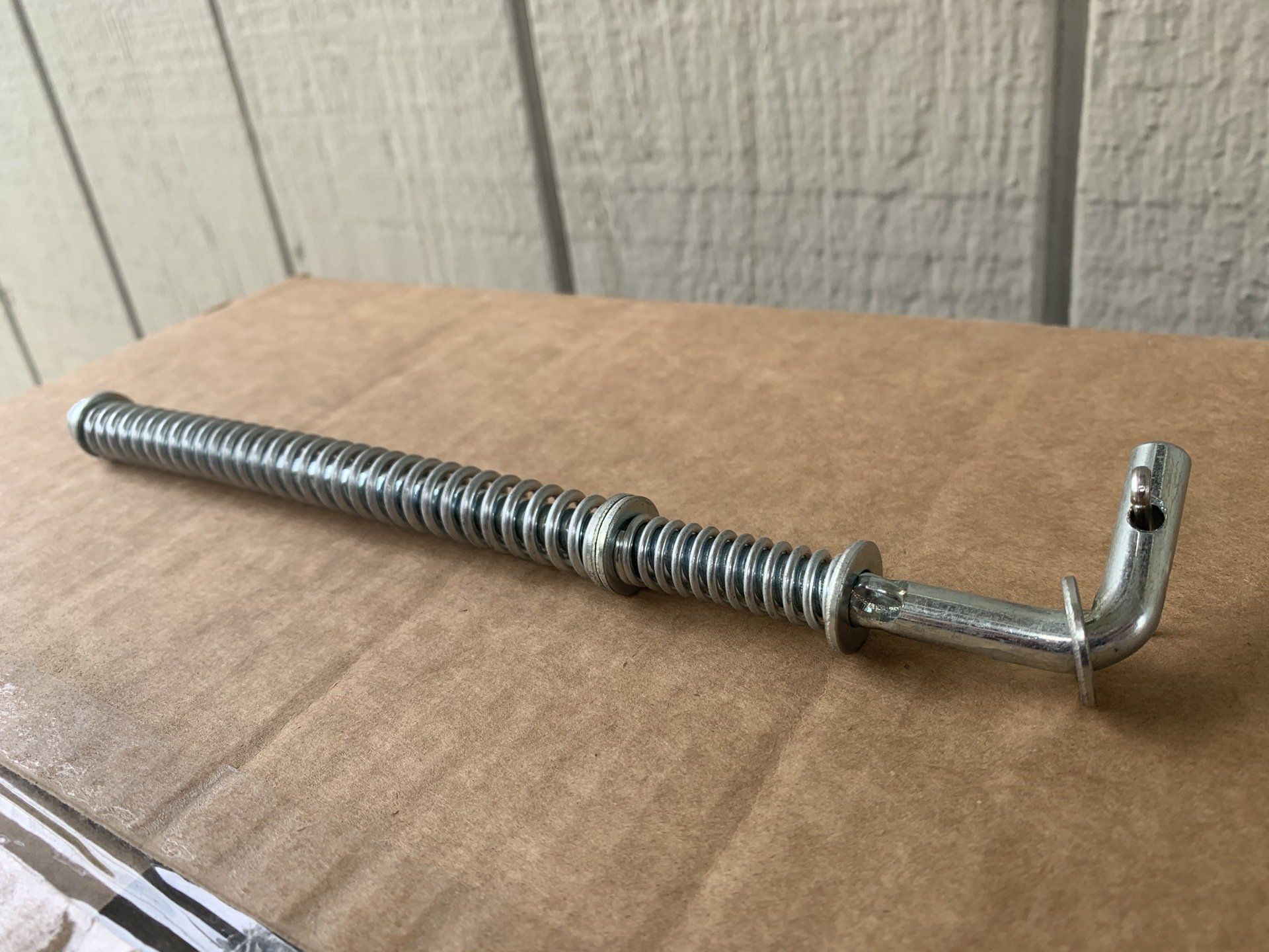 A metal spring assembly with a curved end, lying on cardboard.