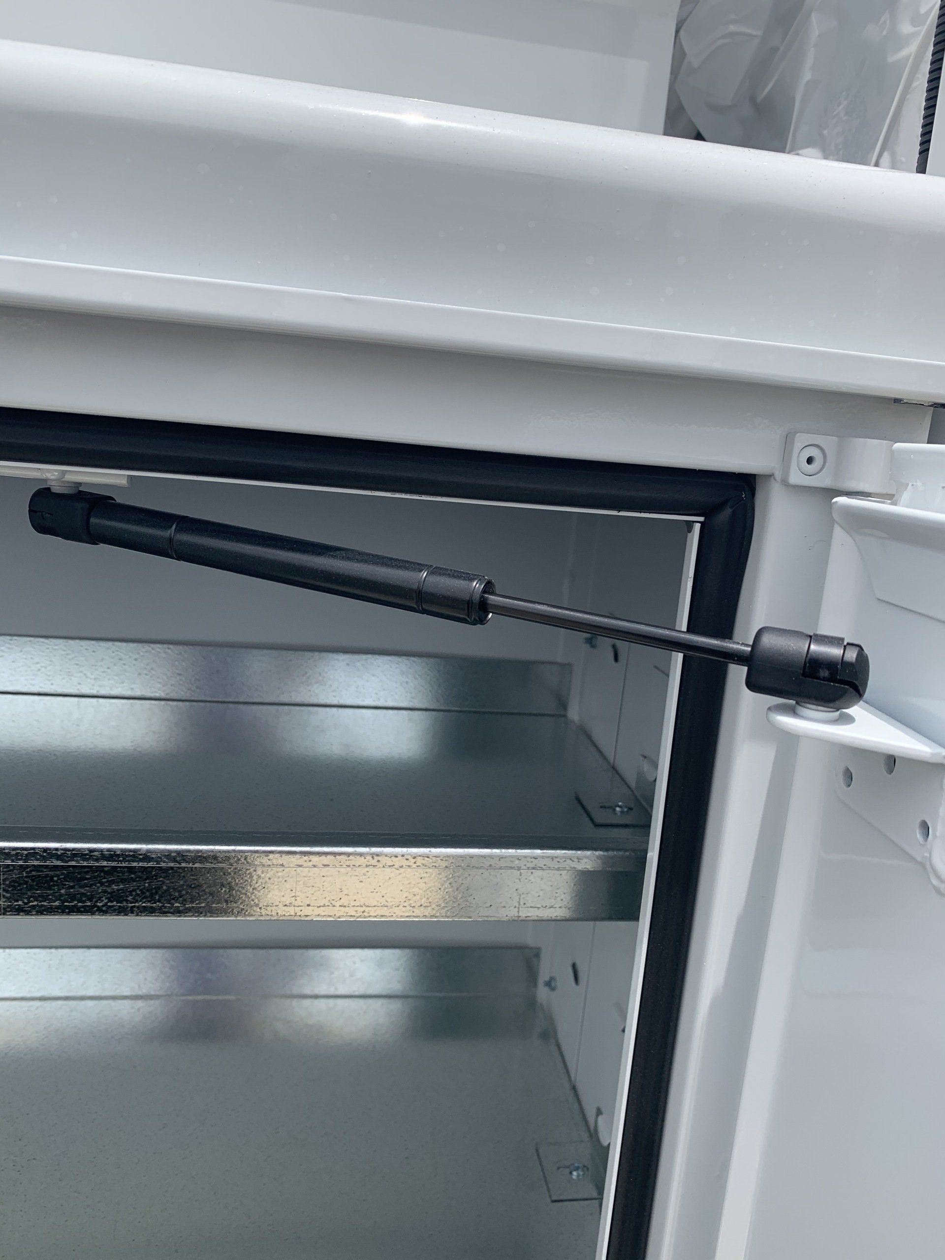 White cabinet door with a black gas strut holding it open, revealing shelves.