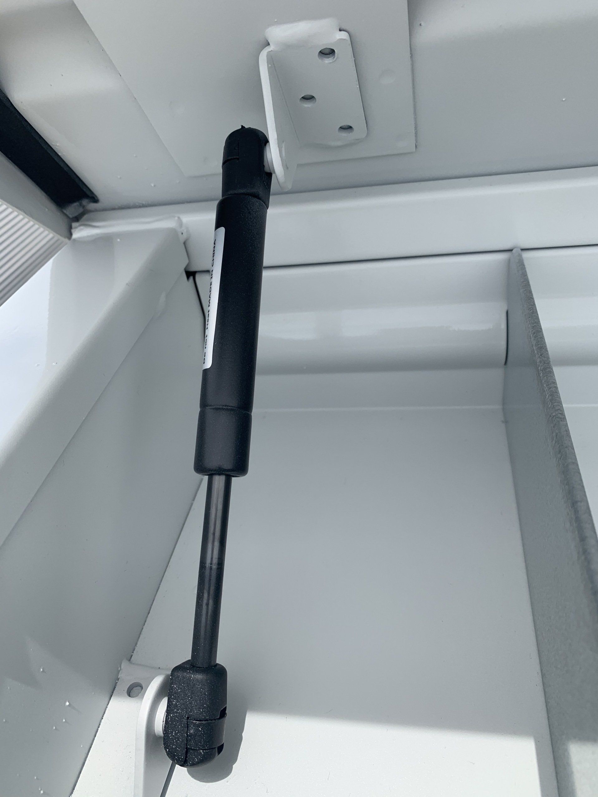 Black gas strut attached to a white compartment, supporting an open door.