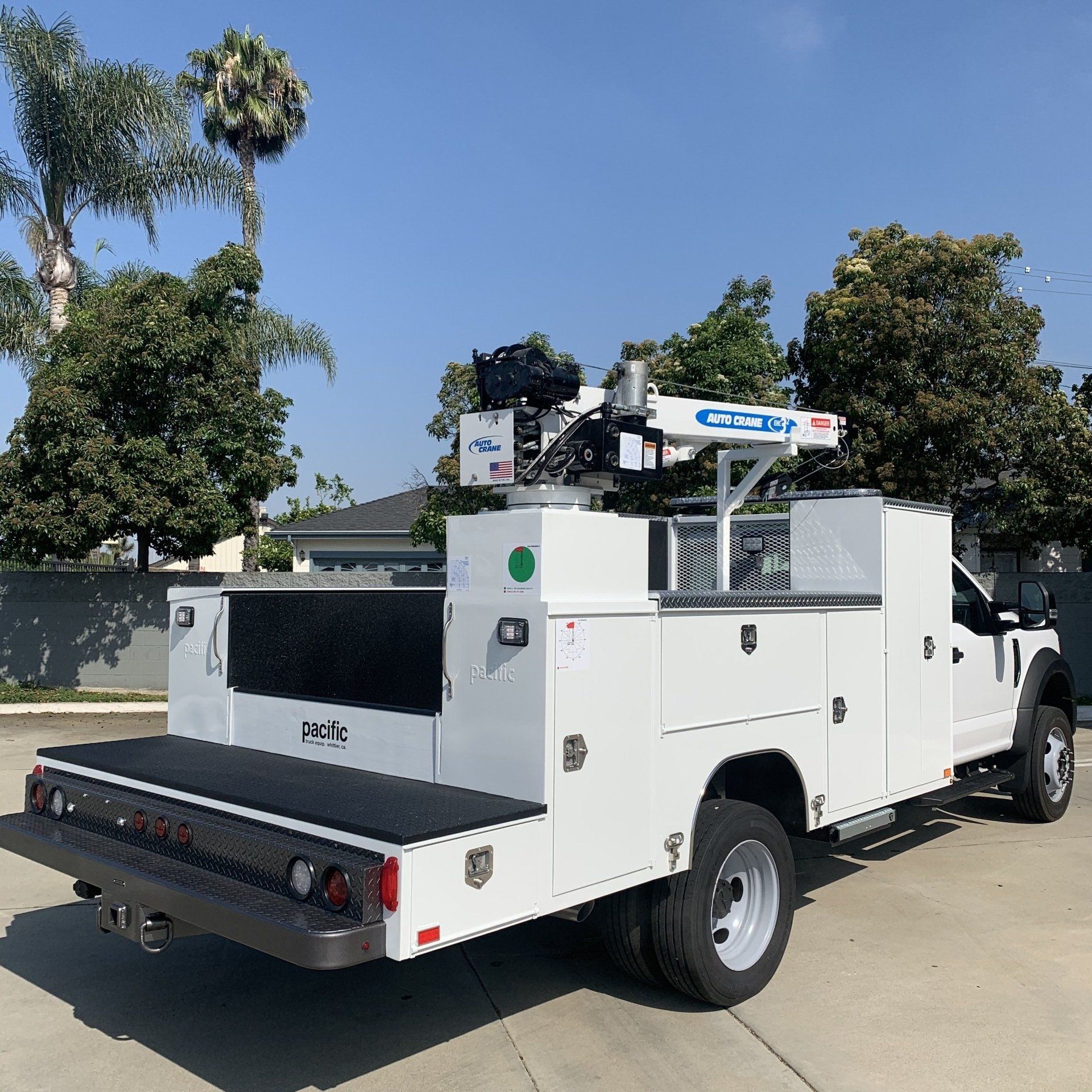 White utility truck with crane, parked outside on a sunny day.