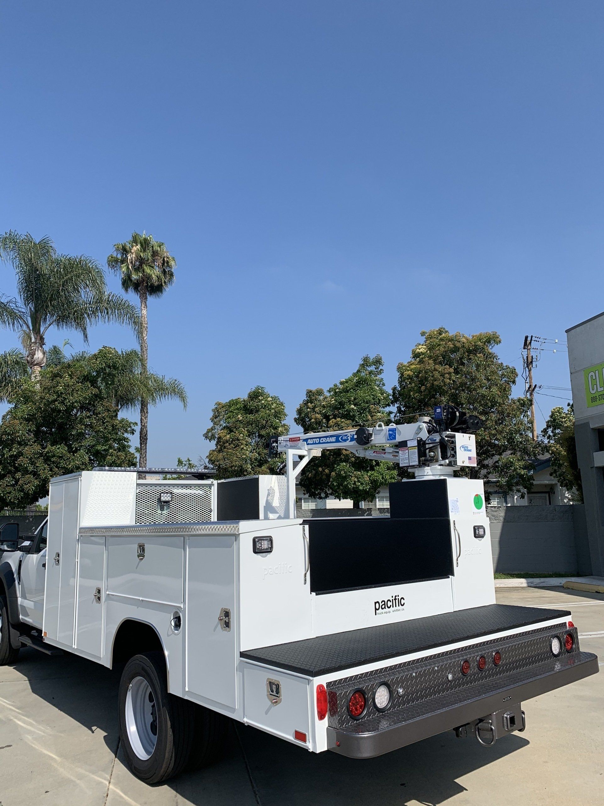 White utility truck with equipment and platform, parked outdoors on a sunny day.
