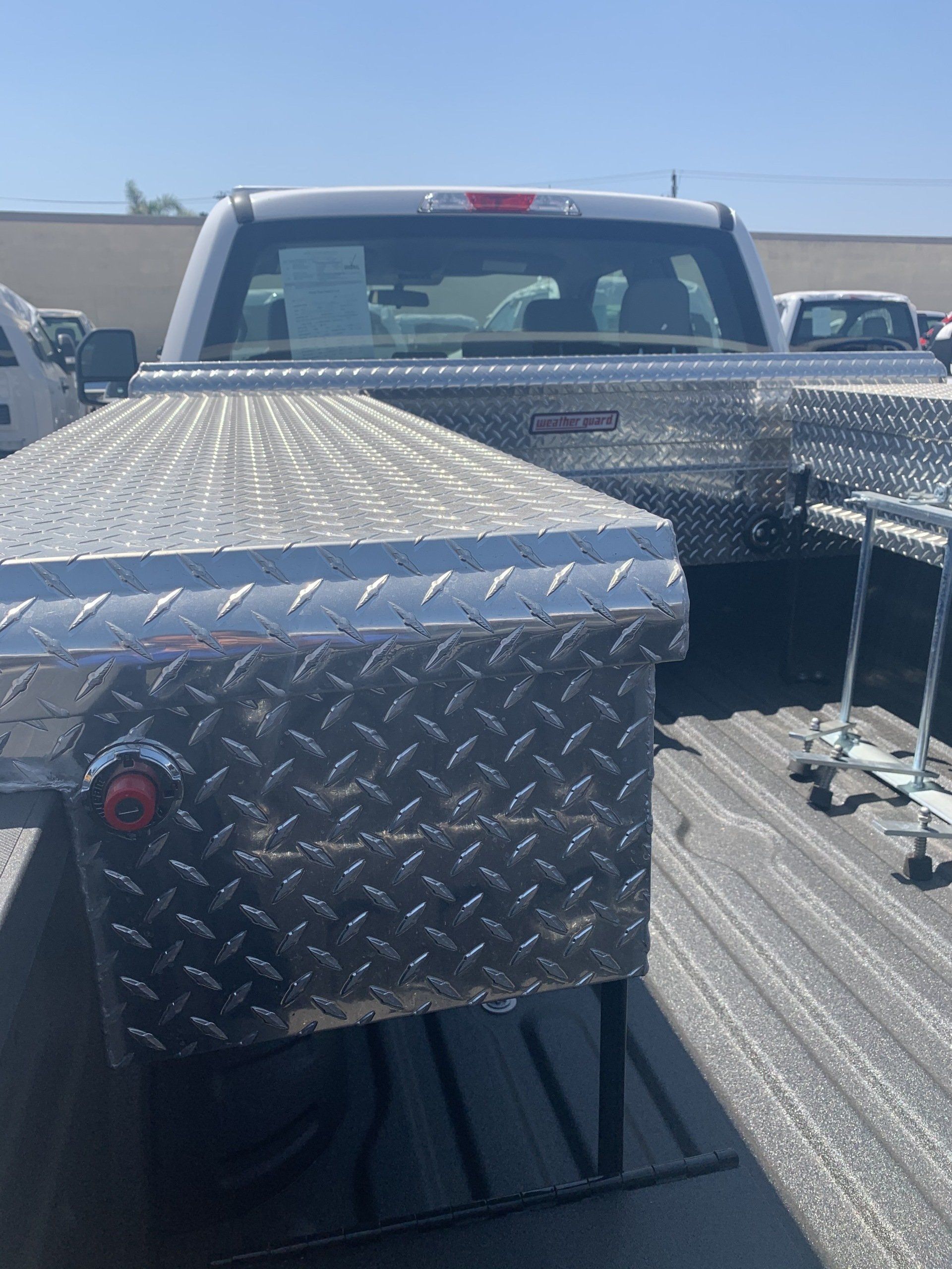Diamond-plated aluminum toolboxes in a truck bed, in front of a white pickup truck.