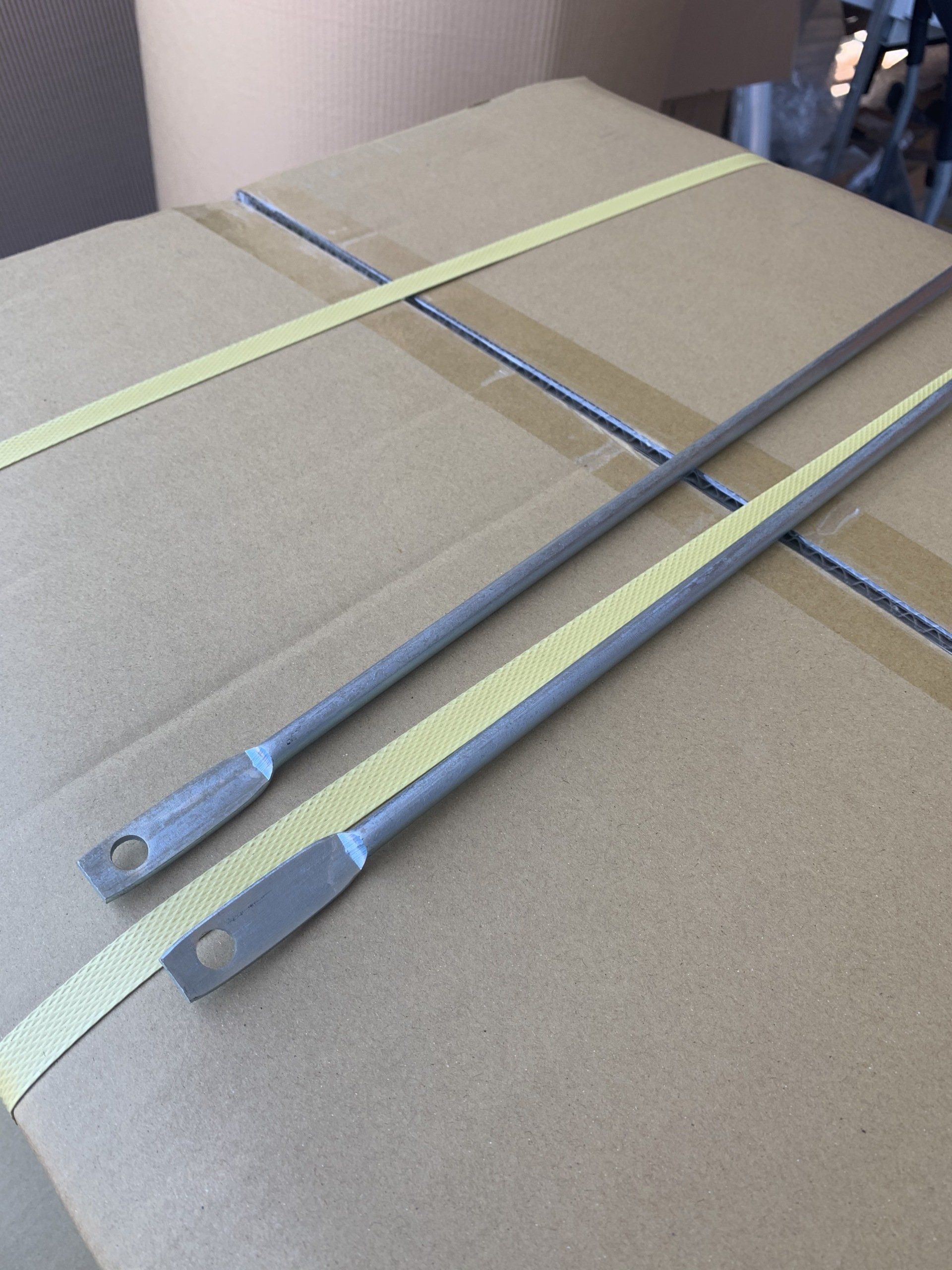 Two metal bars with holes, resting on a cardboard box secured with yellow tape.