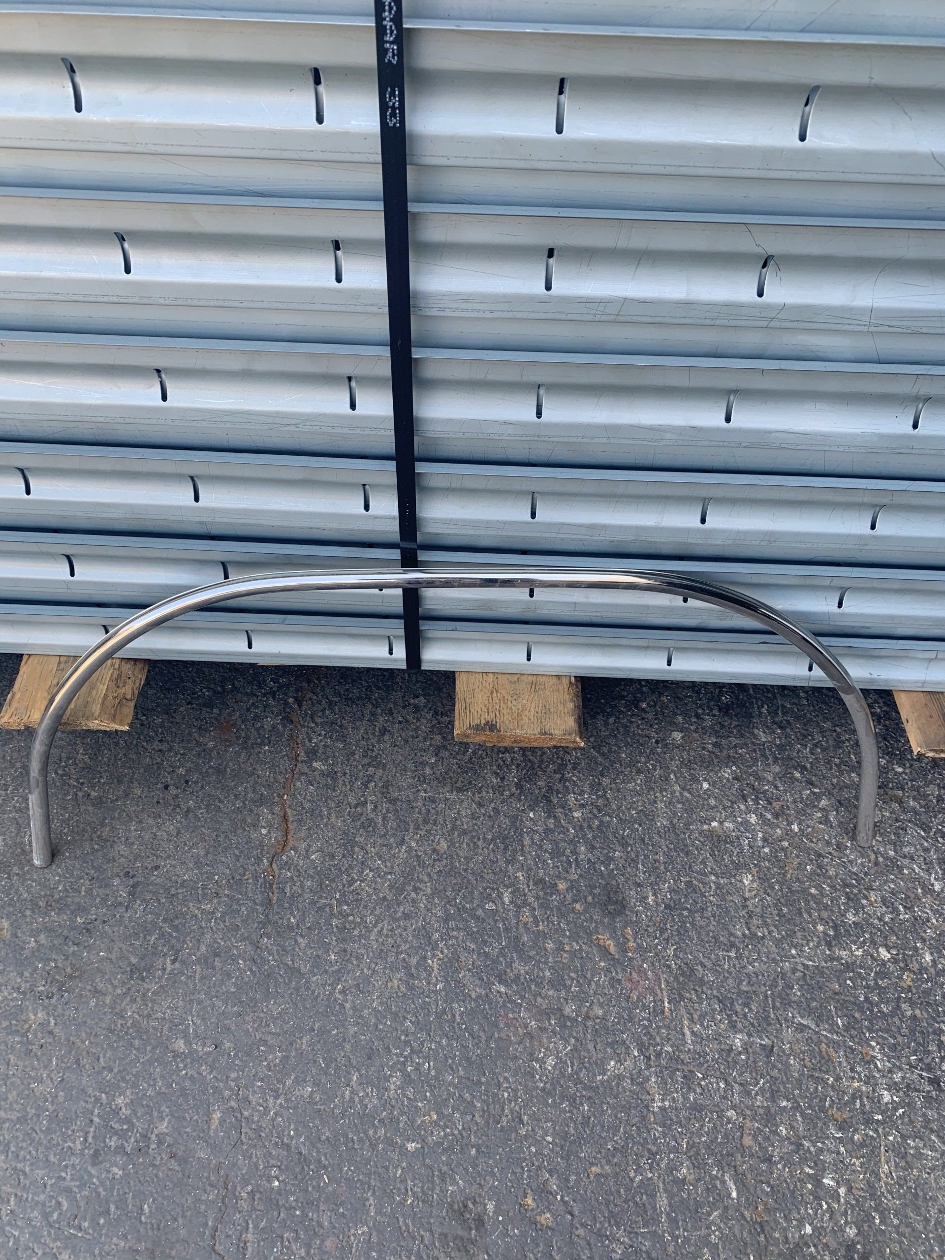 Chrome car bumper on a pallet, stacked metal sheets in the background.