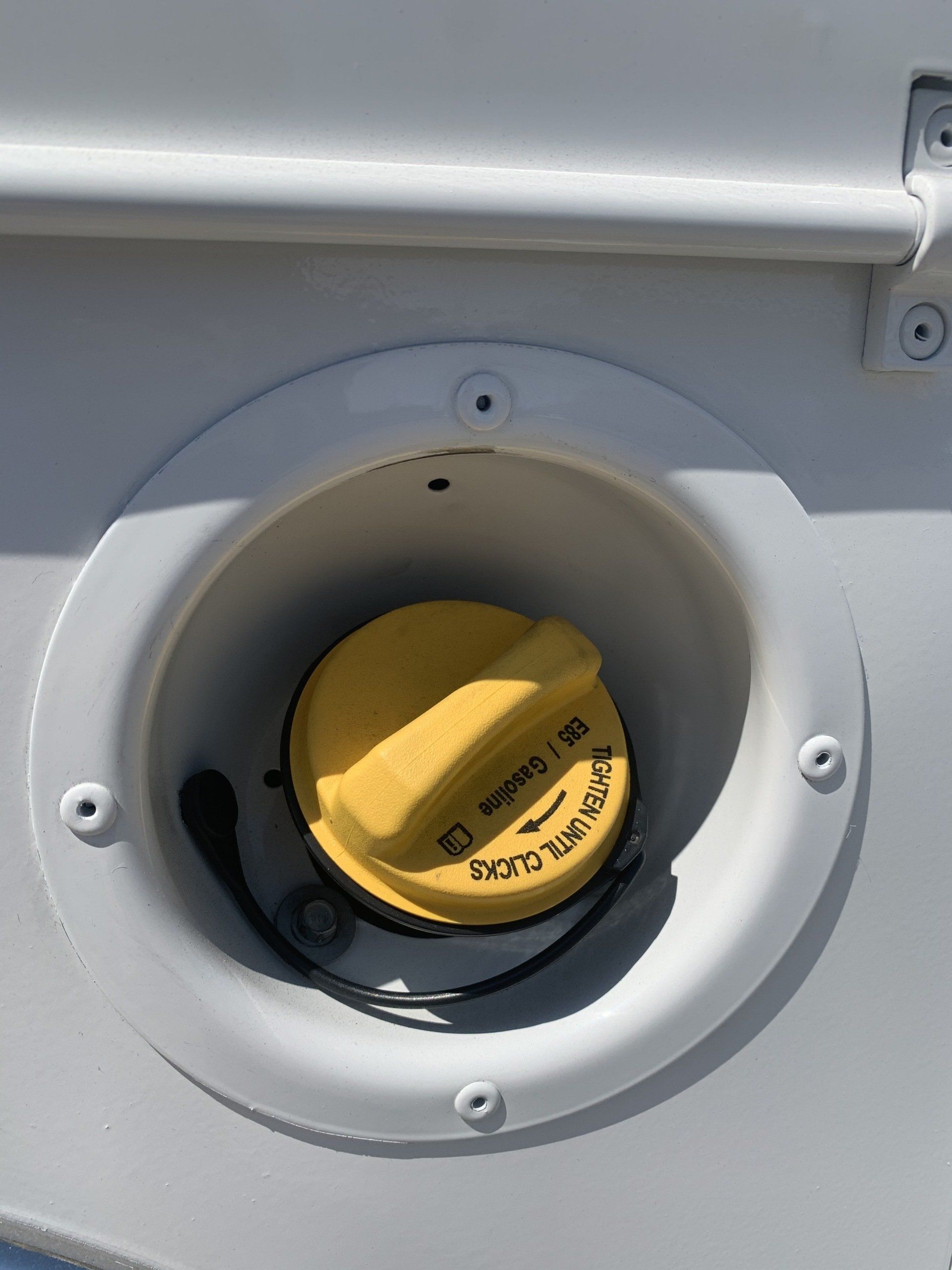 Yellow fuel cap in a white housing on a vehicle, with a black tether.