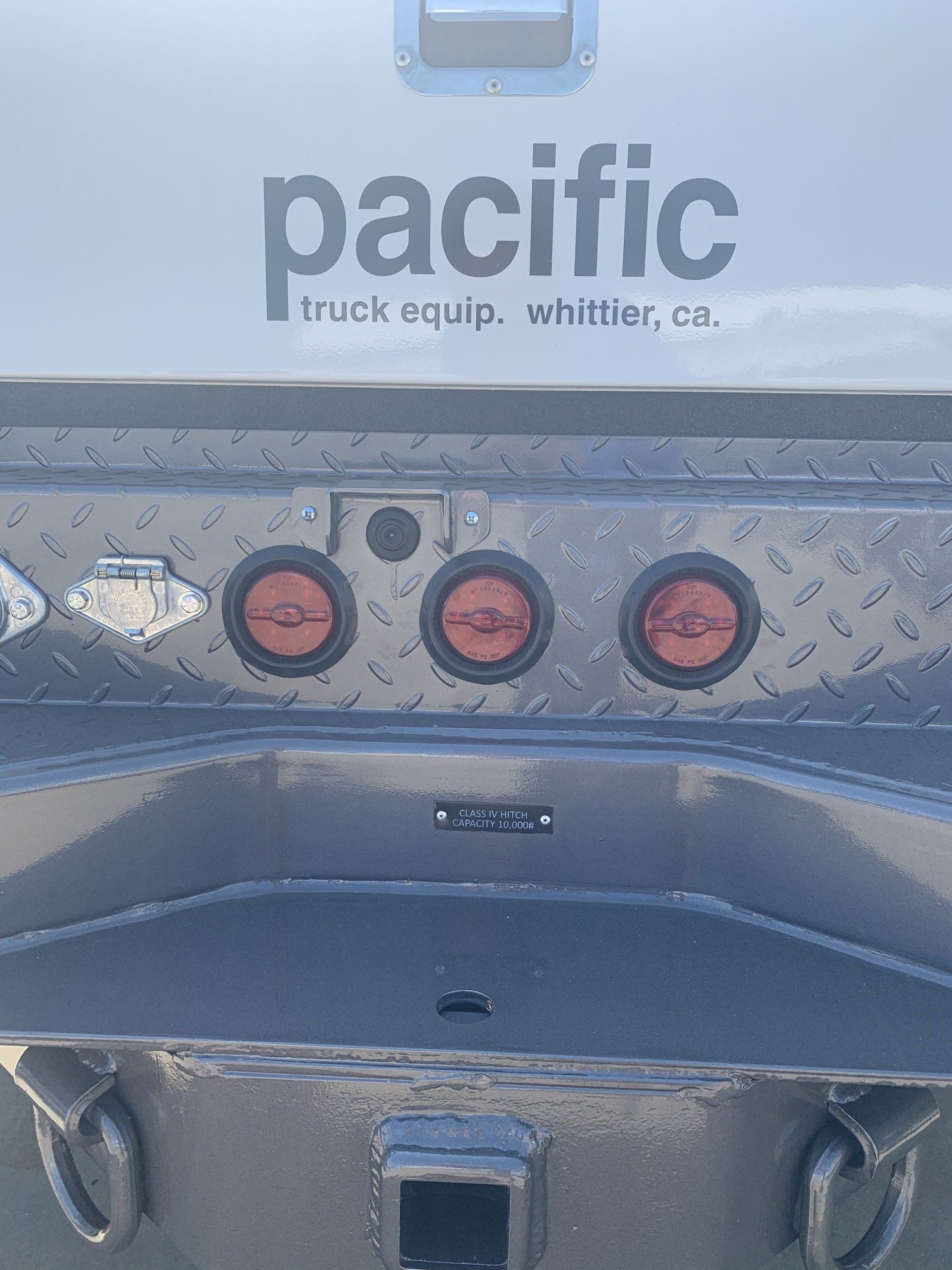 Gray truck bed with Pacific Truck Equip. logo, three red lights, and diamond plate detailing.