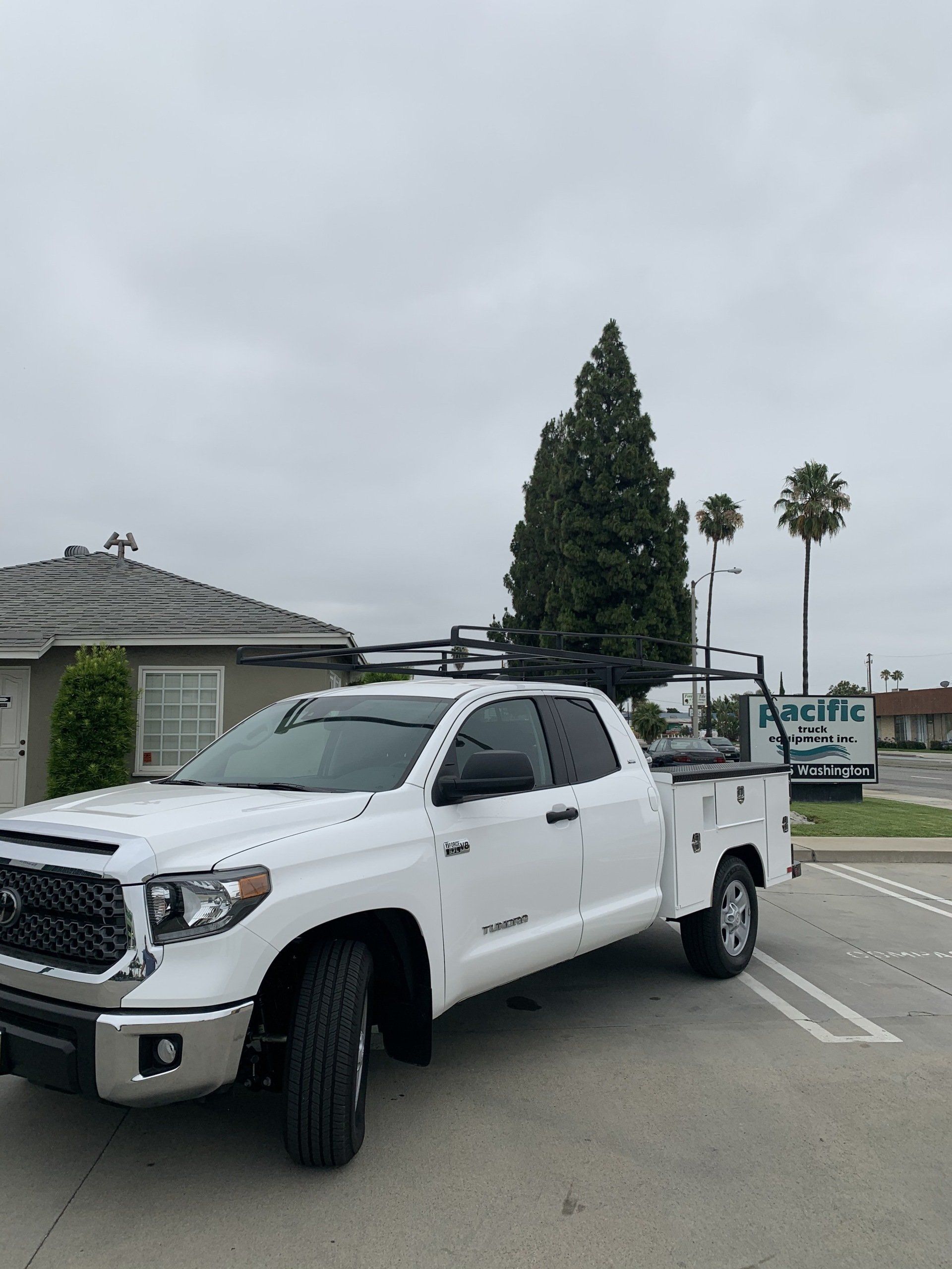 White Toyota Tundra truck with a ladder rack parked outdoors under a cloudy sky.