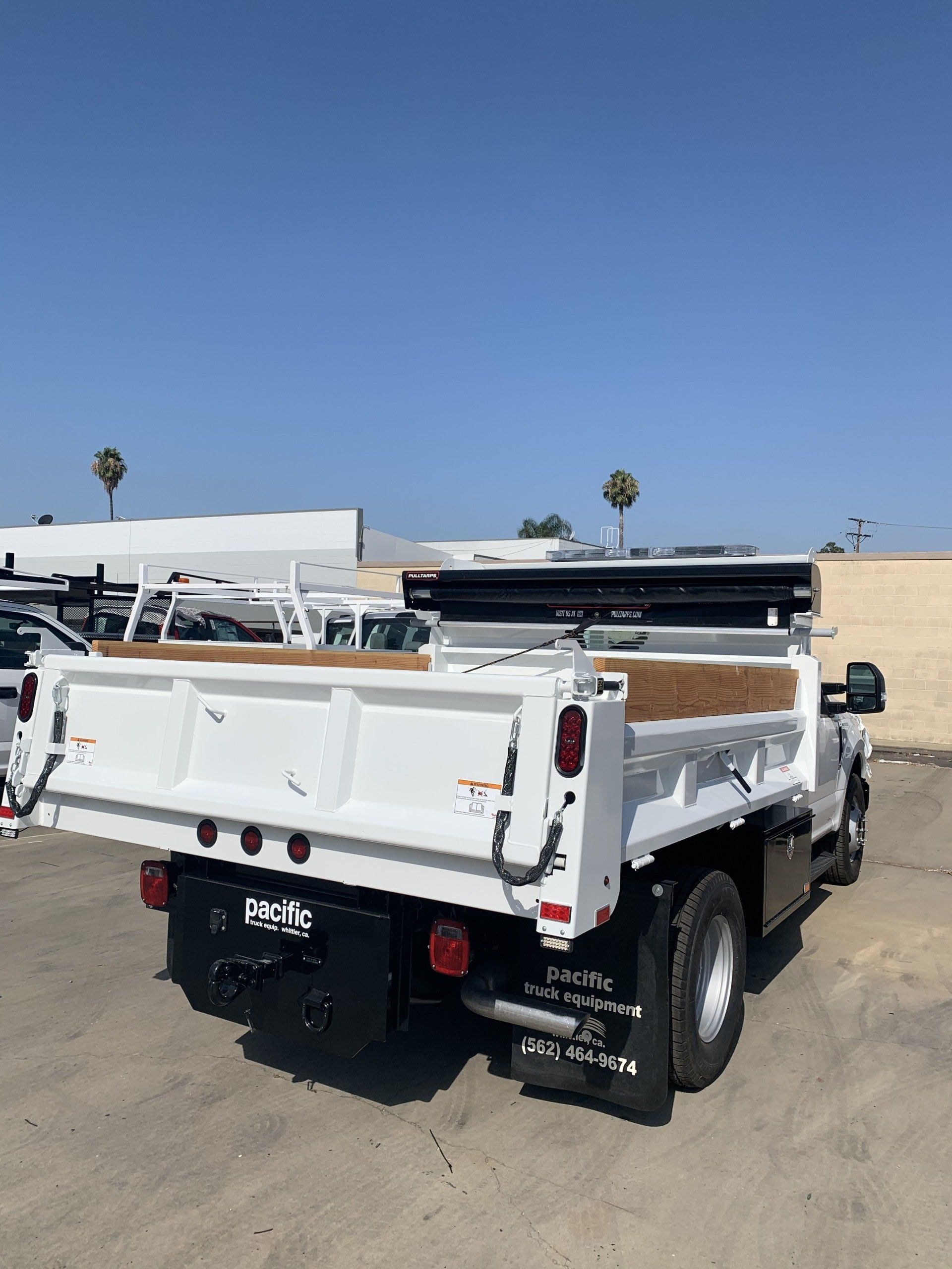 White dump truck with raised bed, black chassis, parked outdoors on a sunny day.