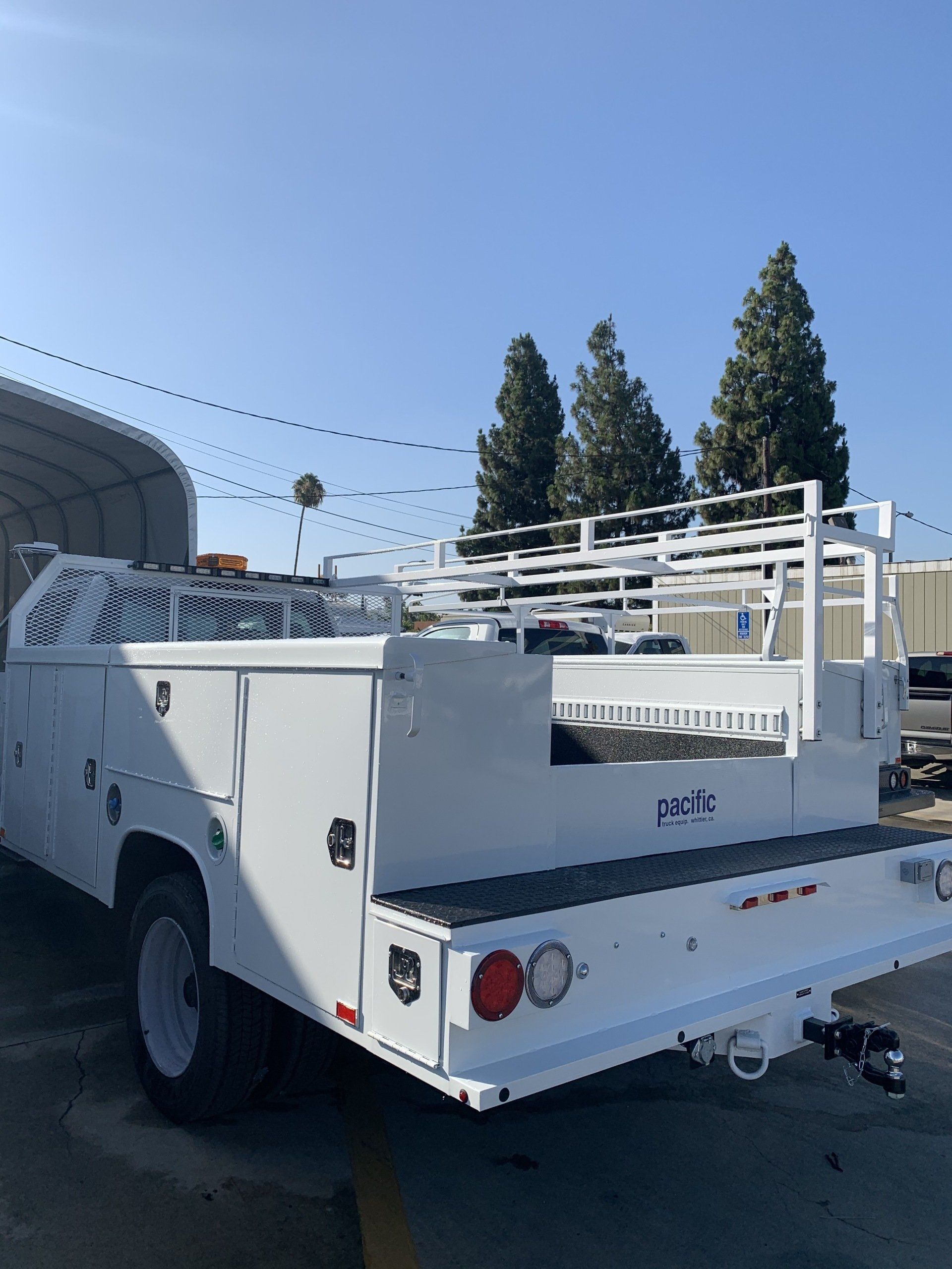 White utility truck with toolboxes and ladder rack in a parking lot.