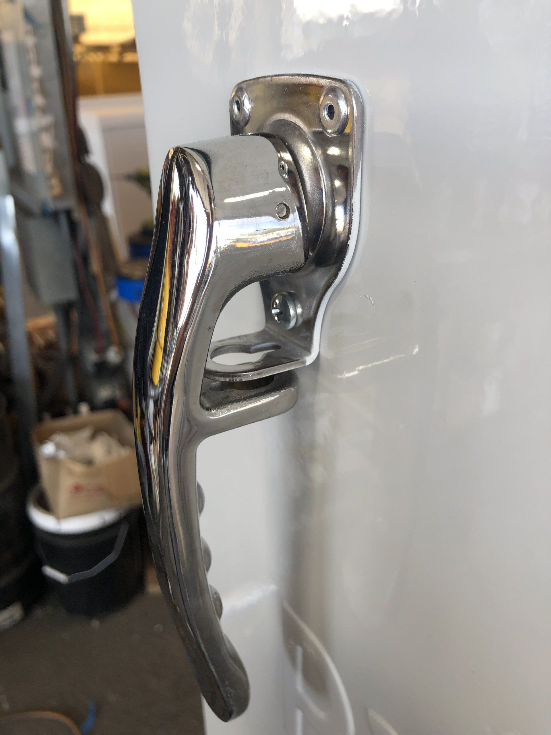 Chrome-colored lever door handle attached to a white surface. The handle is in the closed position.