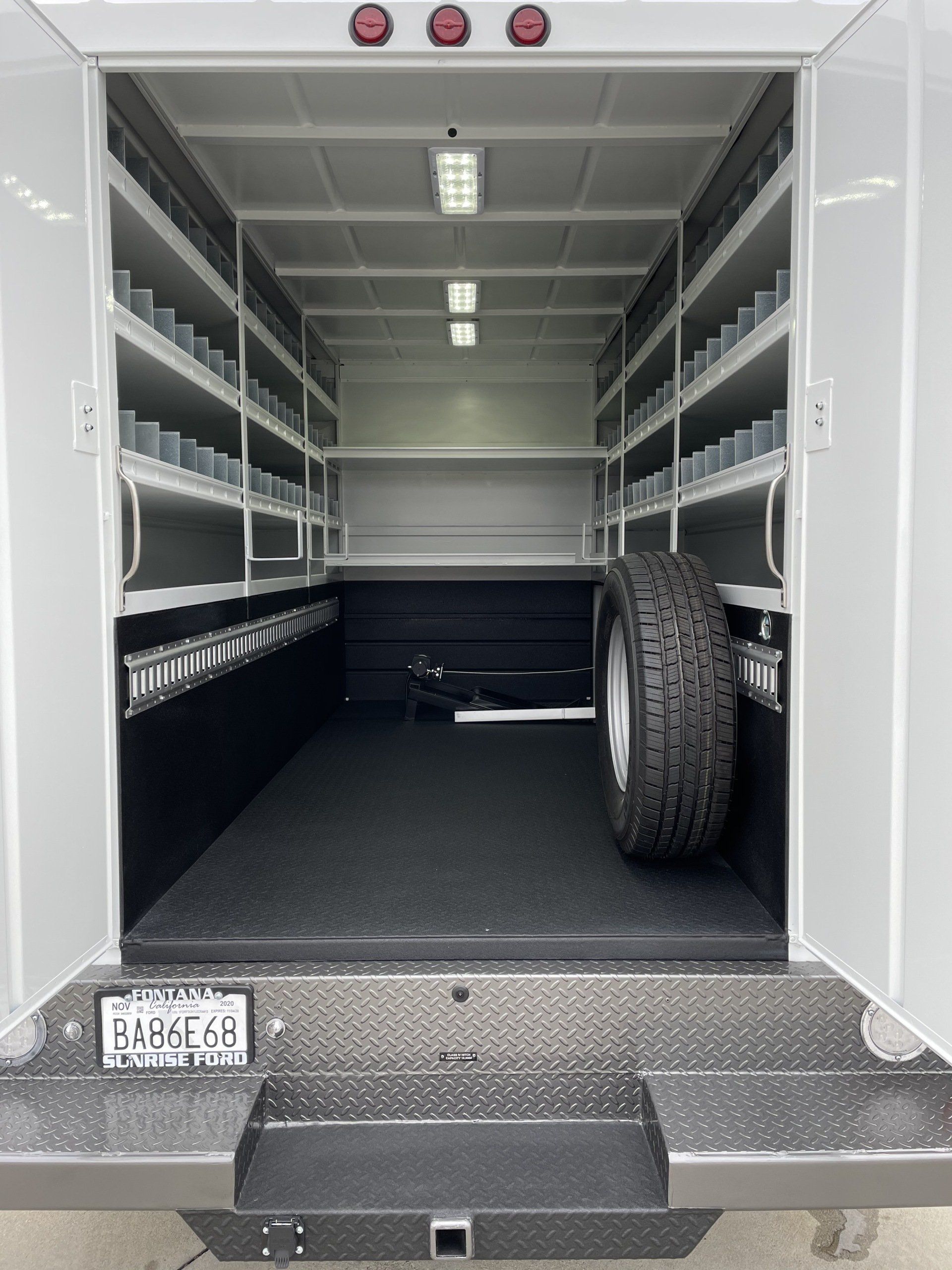 Interior of a white service truck with shelves along the walls, spare tire, and black floor.
