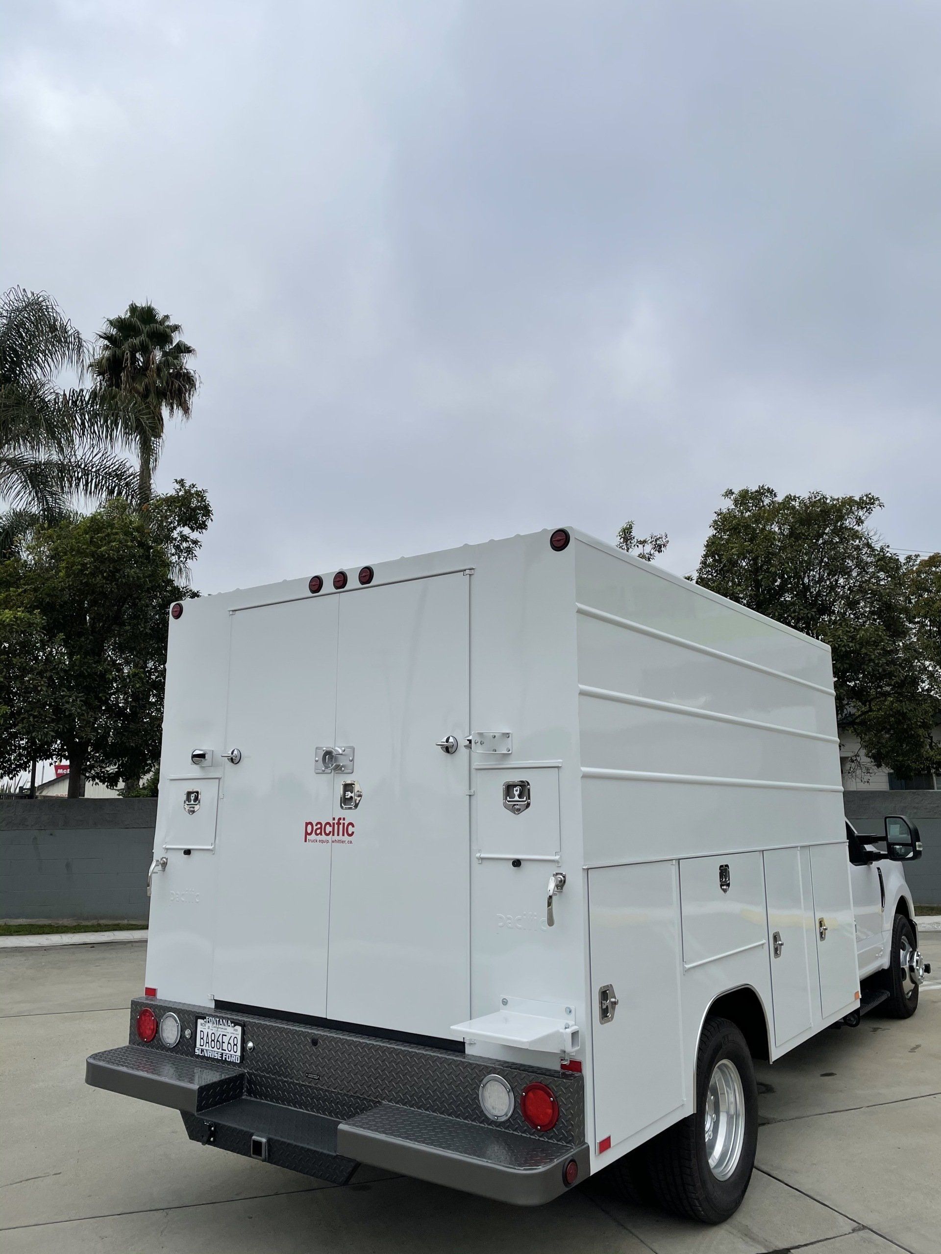 White utility truck with storage compartments under cloudy sky.