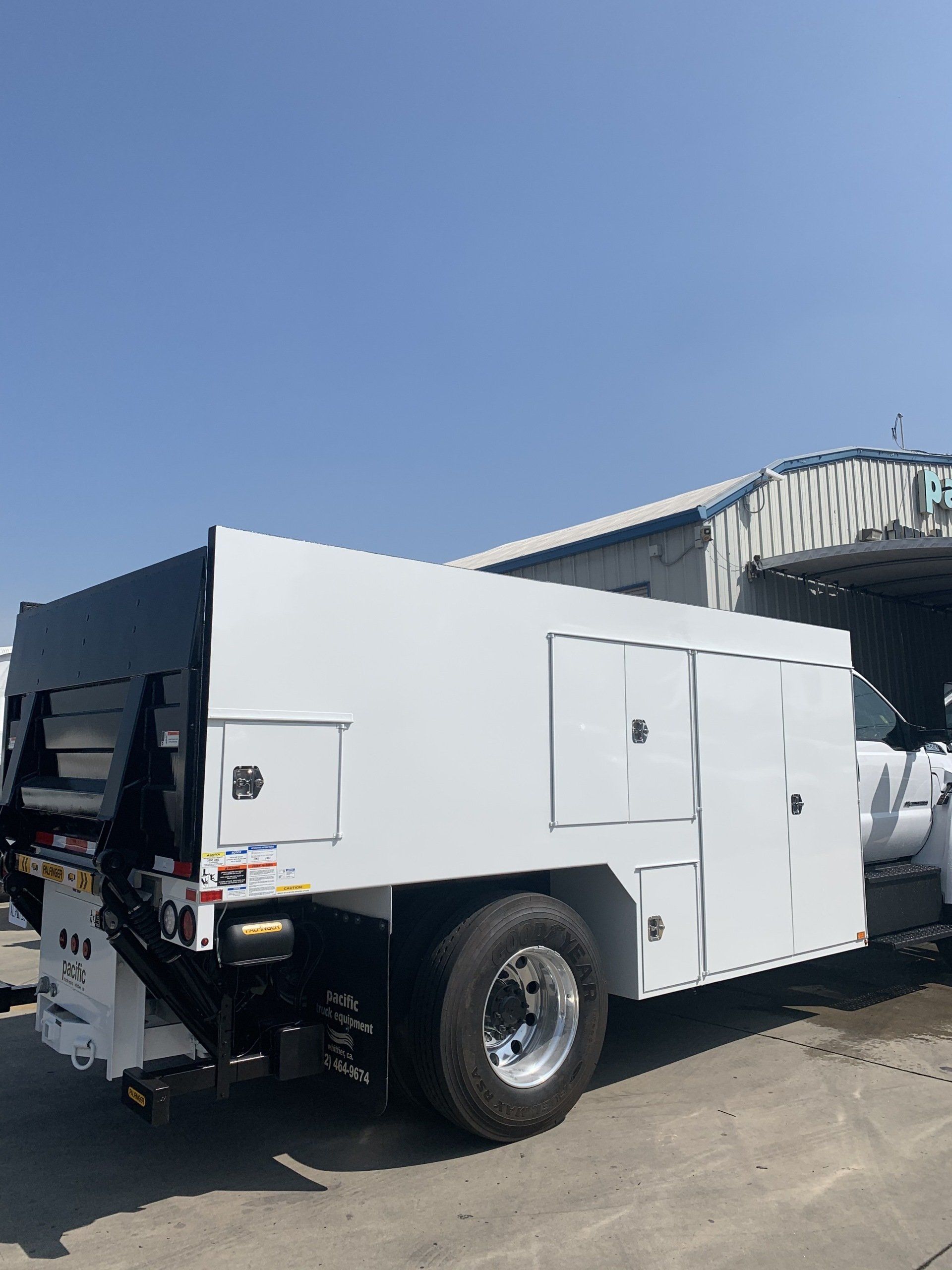 White utility truck with storage compartments under a blue sky.