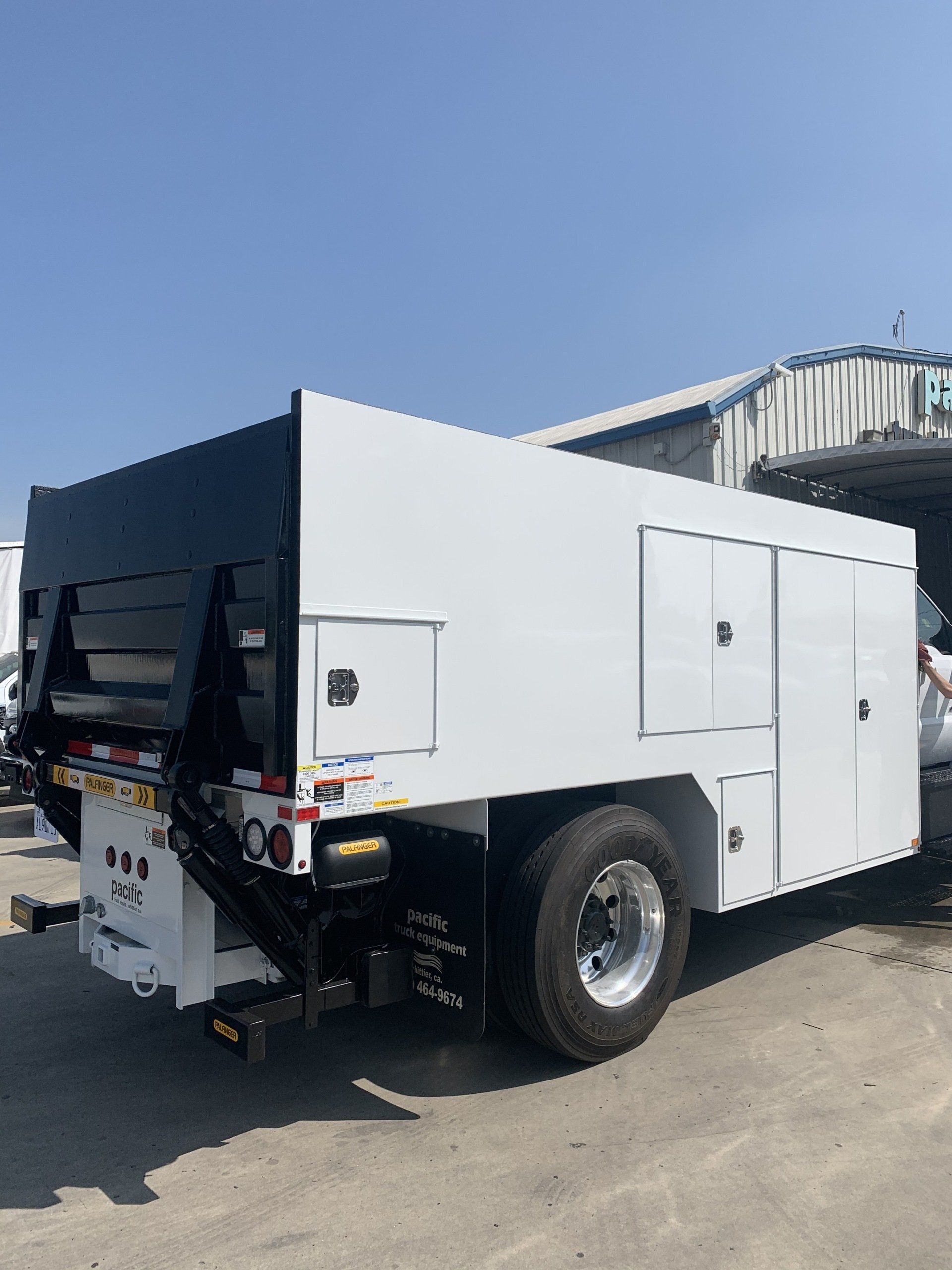 White service truck with black bed and storage compartments, parked outdoors.