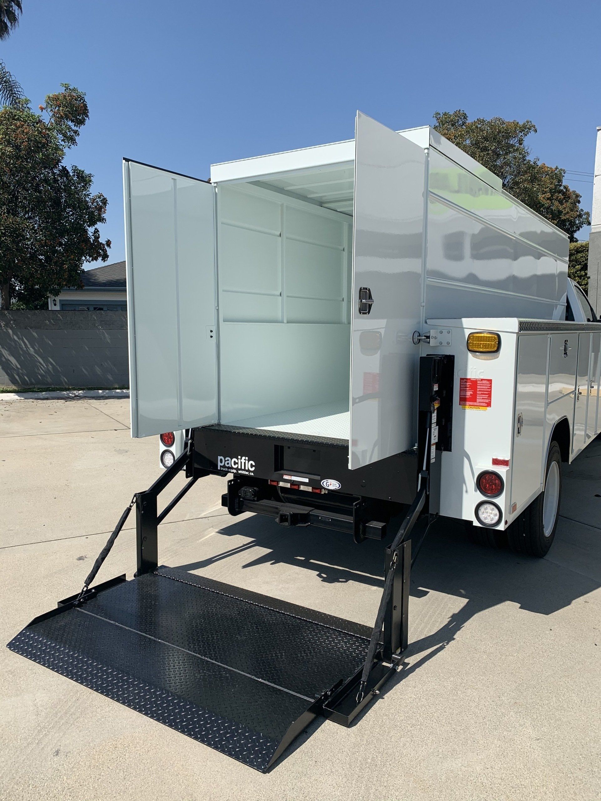 White utility truck with open doors and a ramp, outdoors in daylight.
