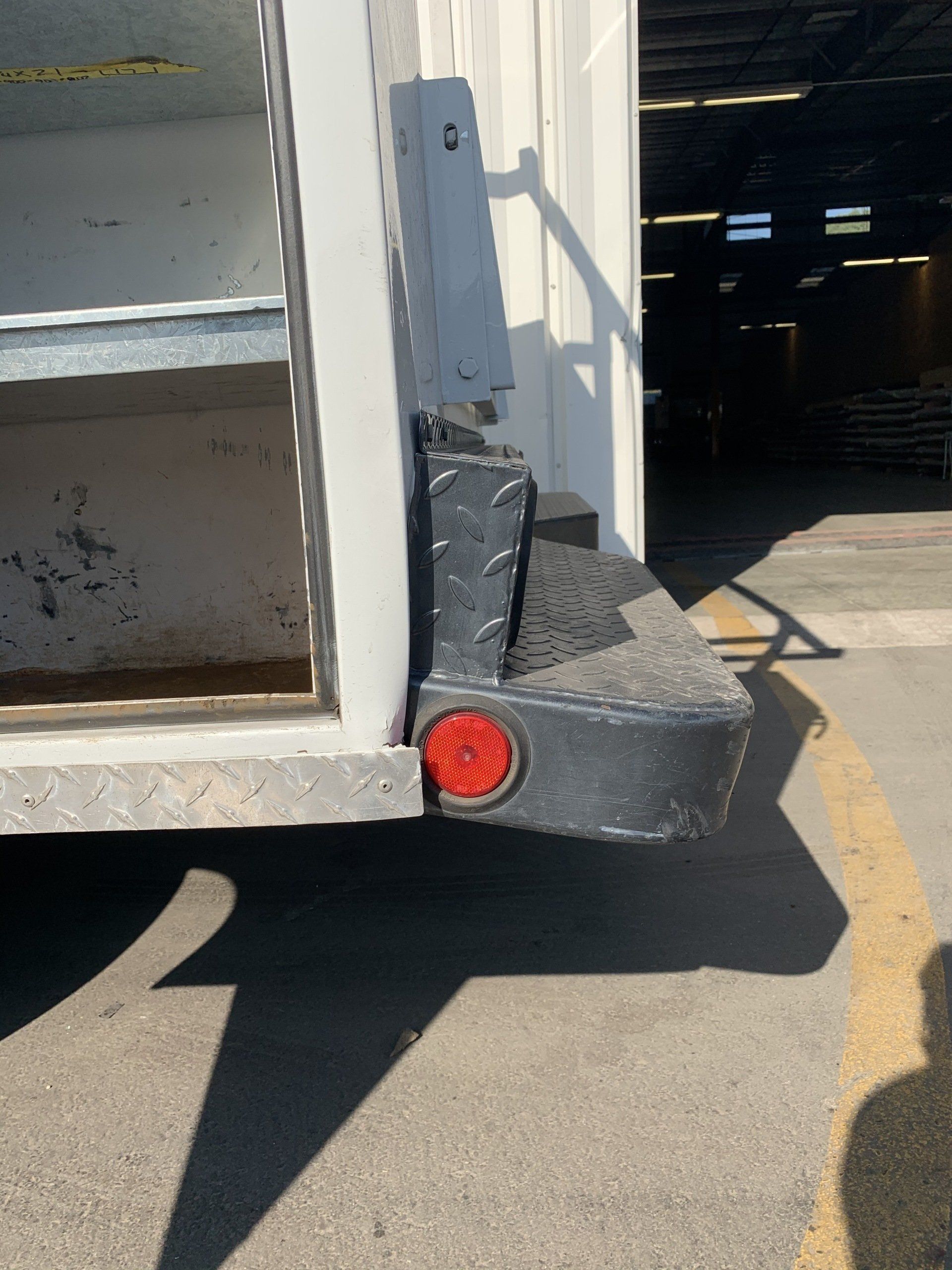 Rear of a white truck with black step and red taillight, parked in a warehouse.