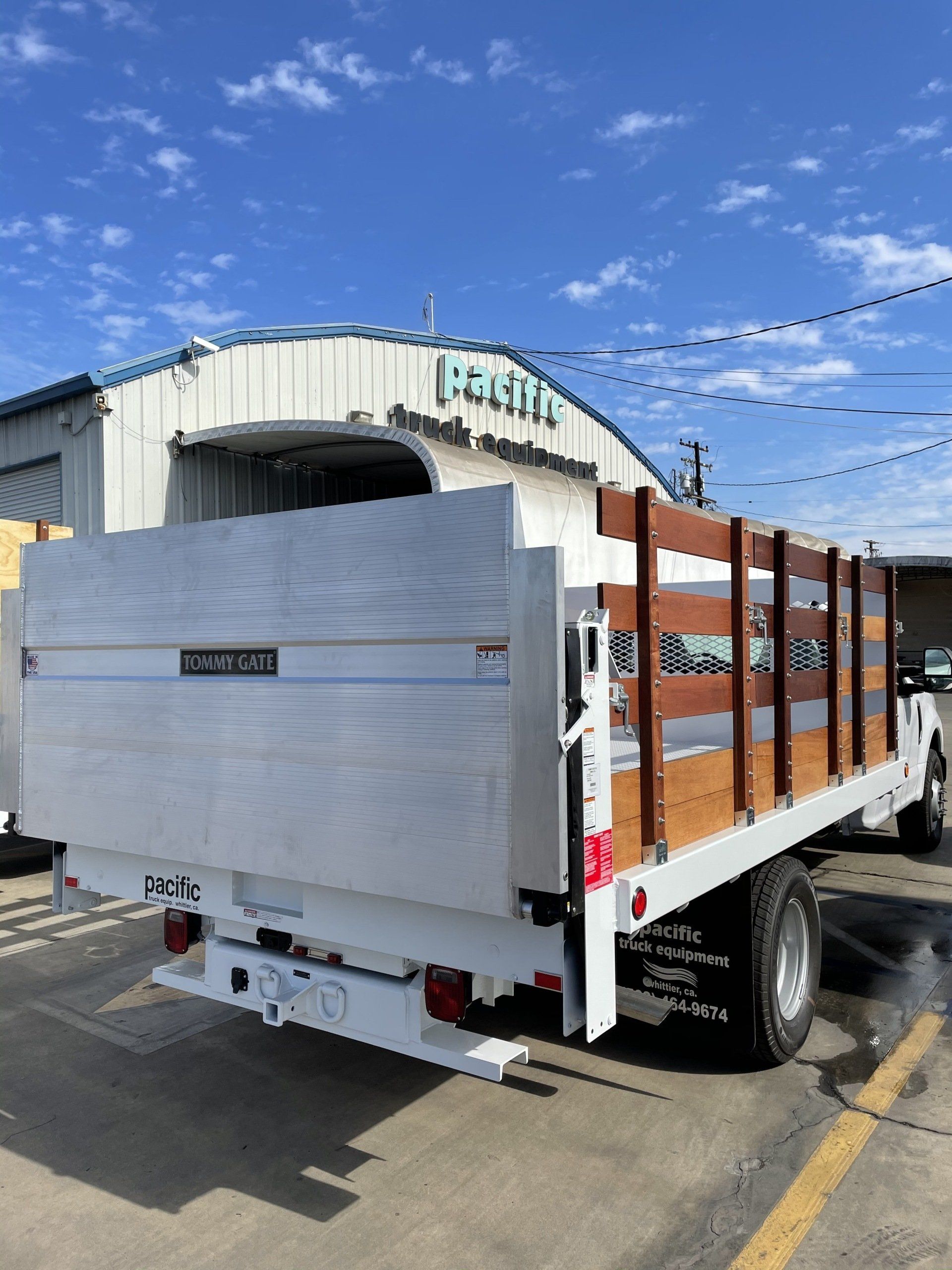 White flatbed truck with wooden side rails parked in front of a building with blue sky.