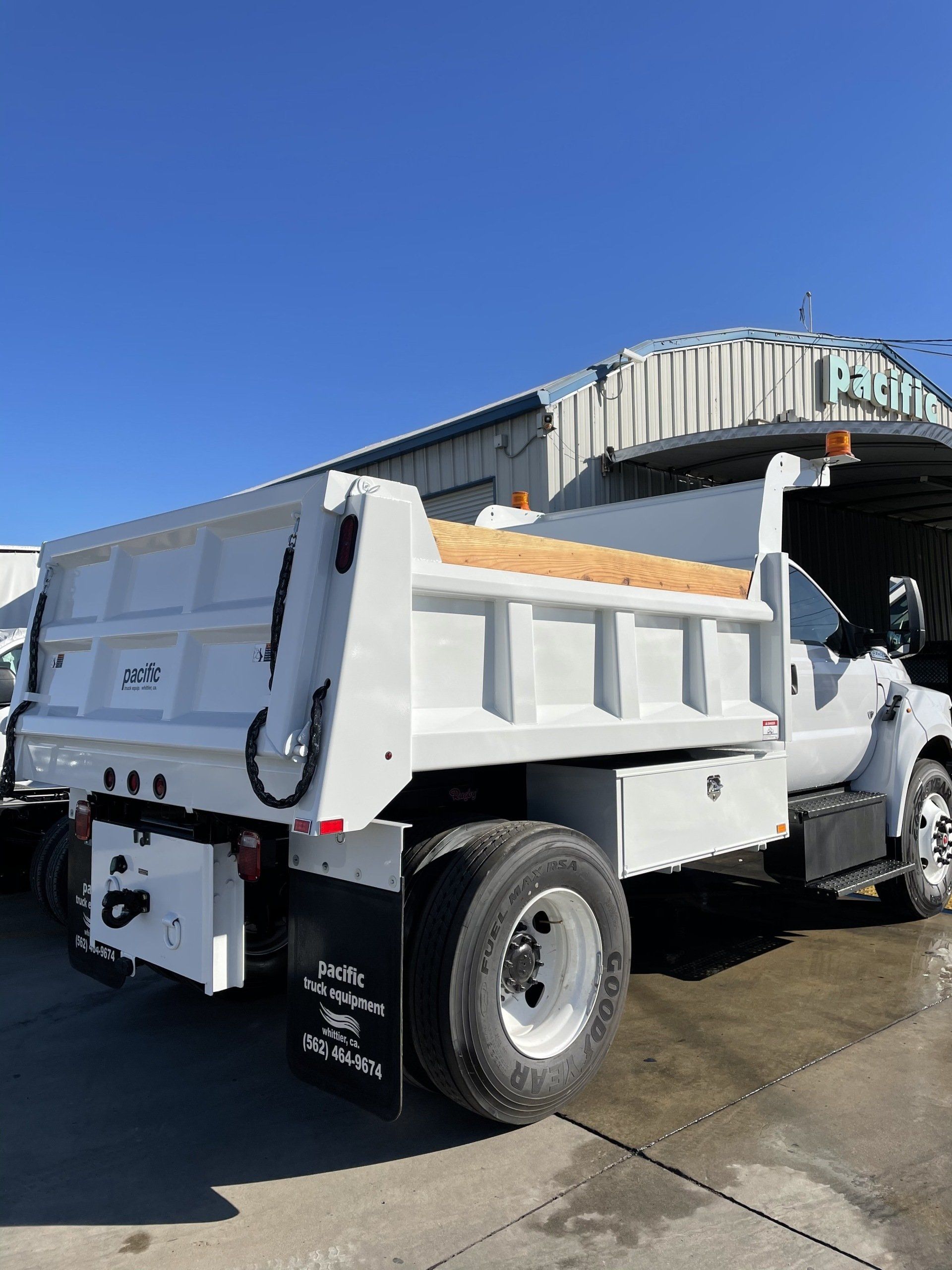 White dump truck with a load of wood, parked outdoors.