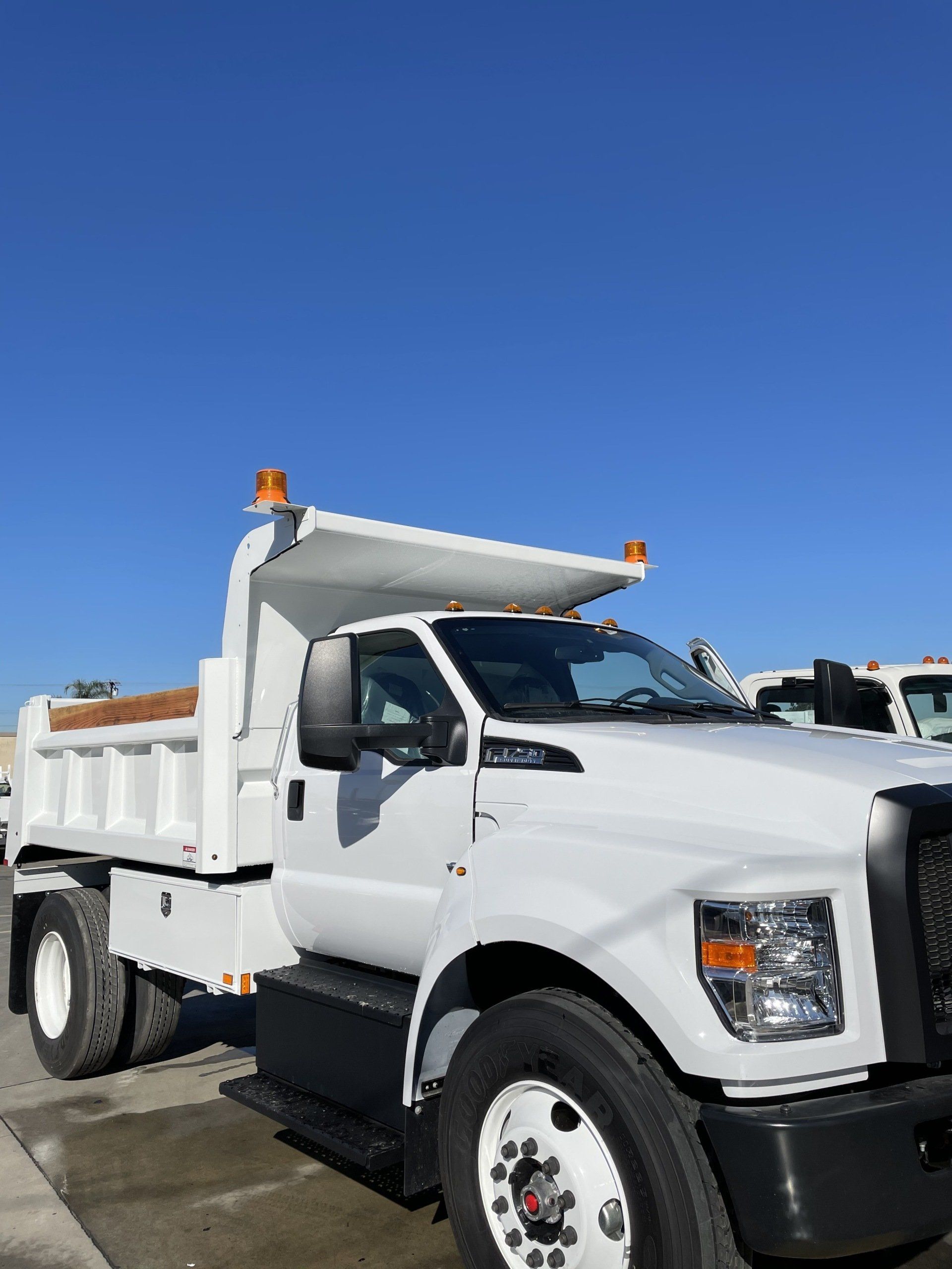 White dump truck under a blue sky, parked outdoors.