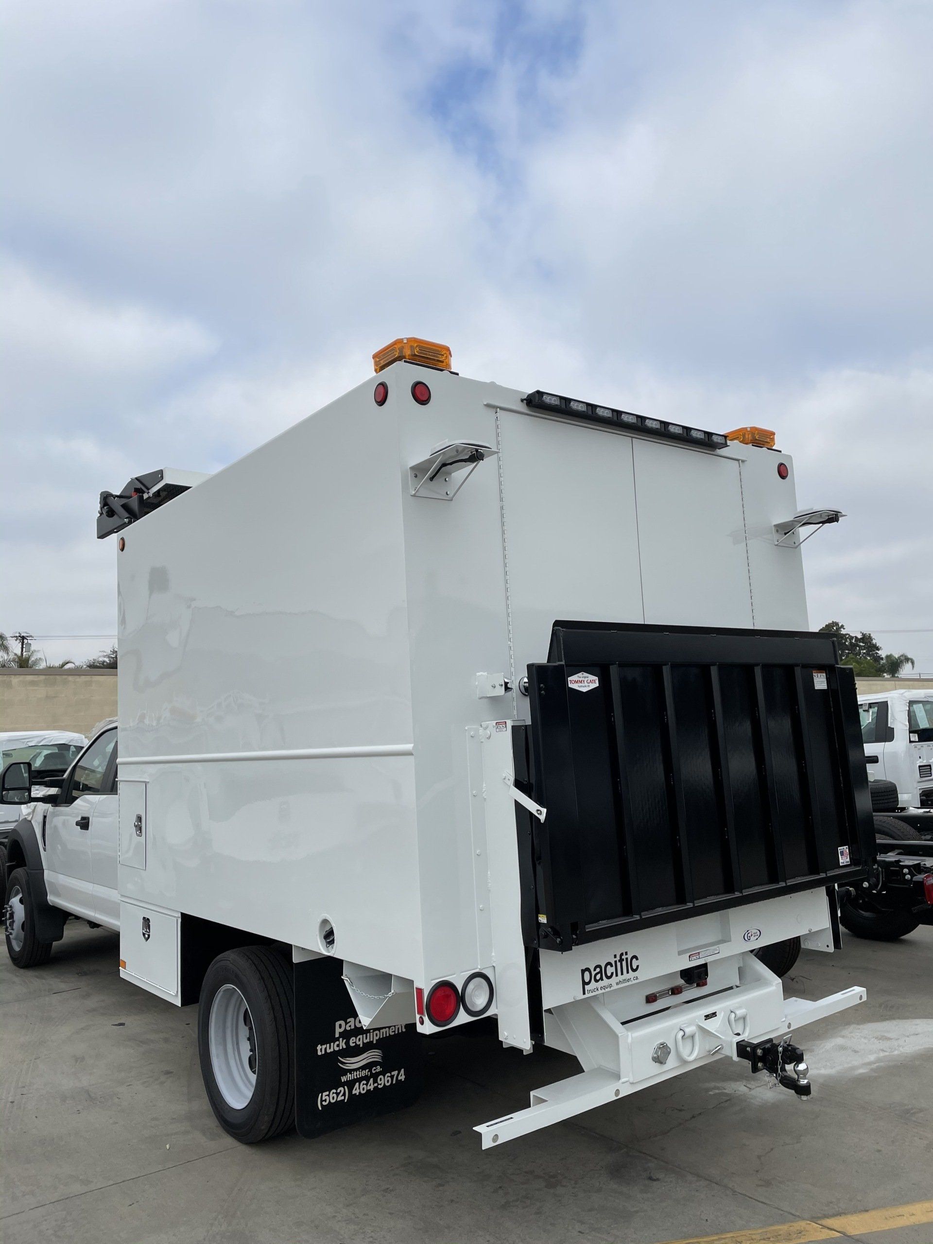 White utility truck with a large enclosed box, back view, under a cloudy sky.