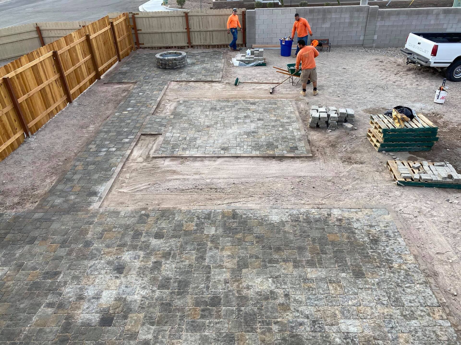 A group of men are working on a patio in a backyard.