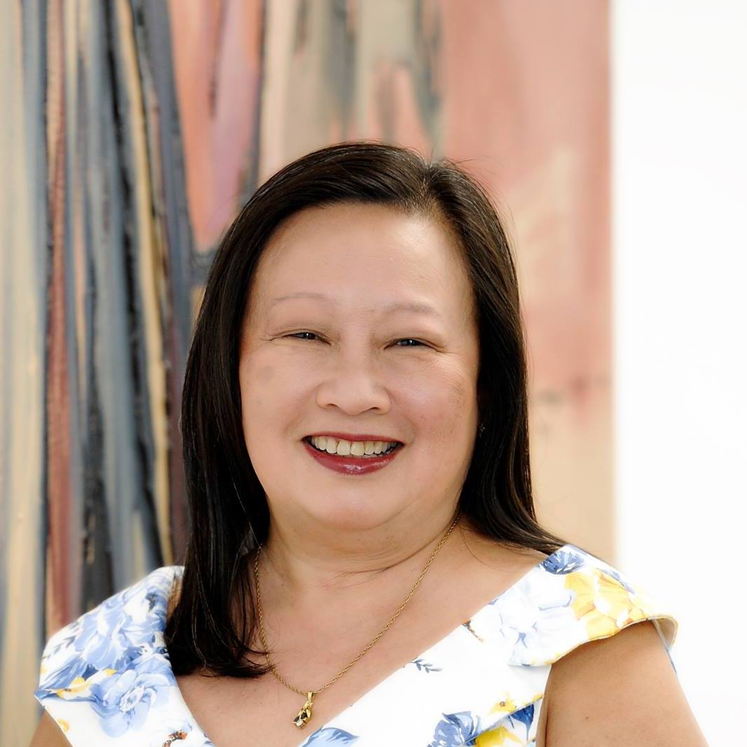 A woman in a floral dress is smiling in front of a painting.