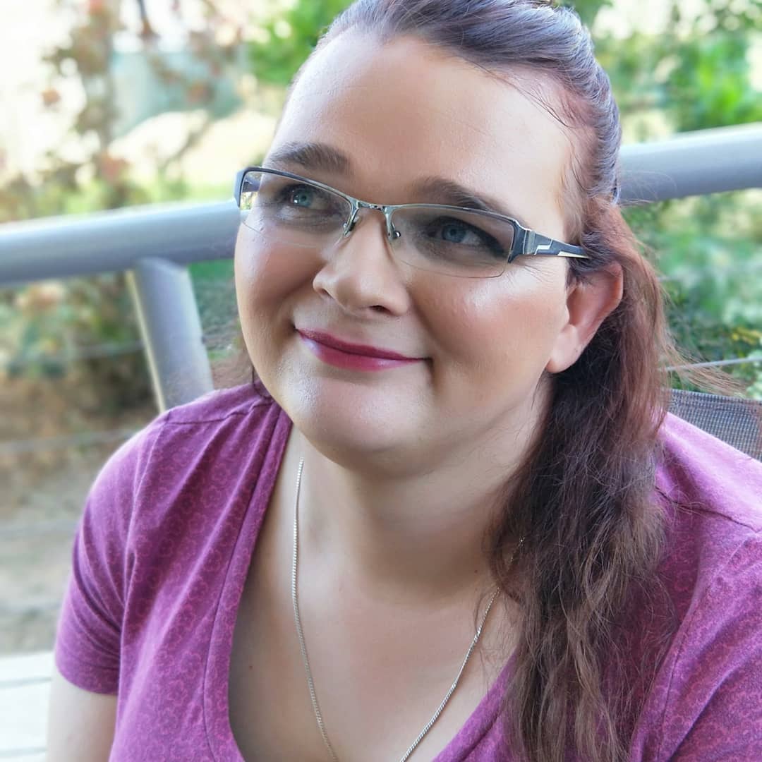 A woman wearing glasses and a purple shirt is smiling.