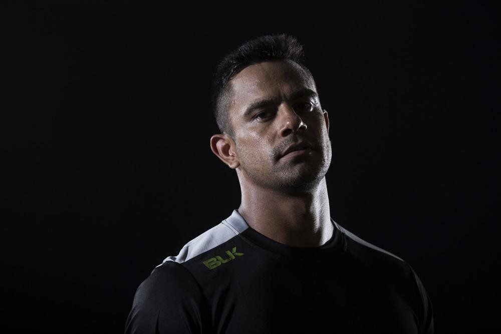 A man in a black shirt is standing in the dark and looking at the camera.