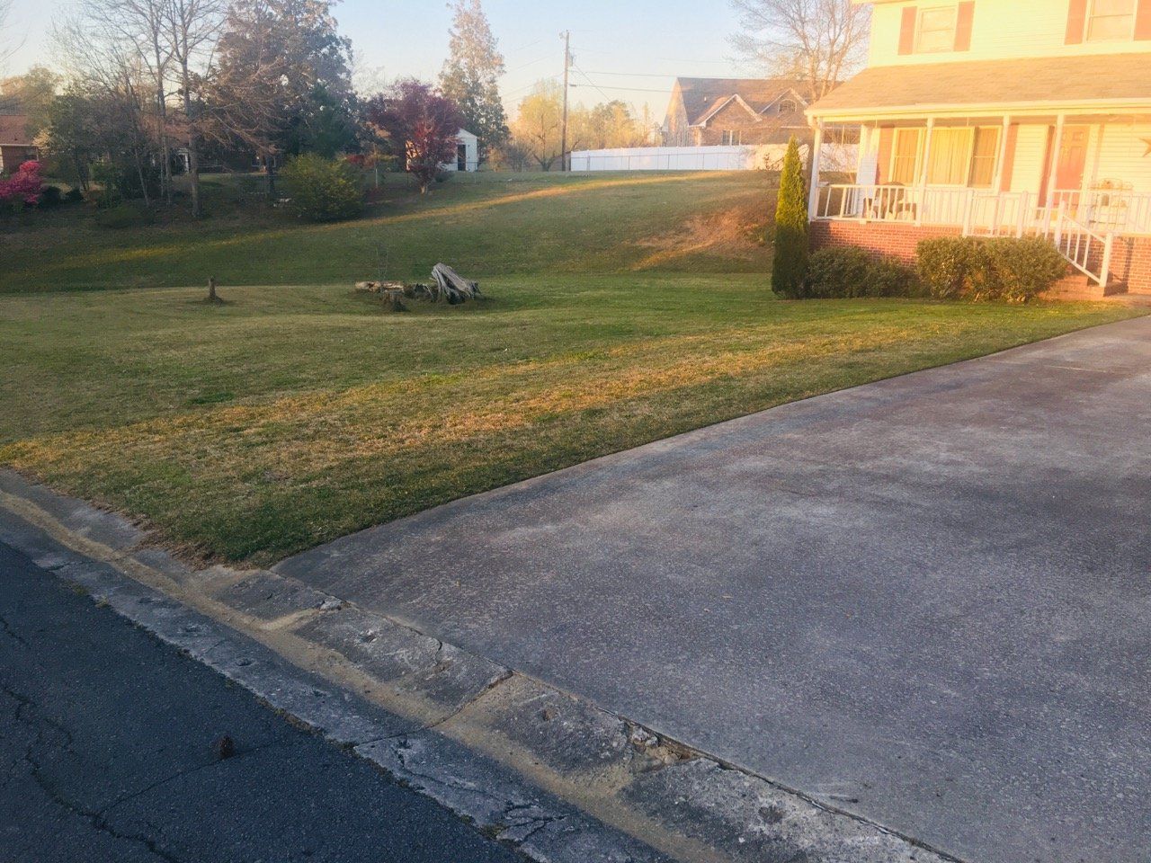 A house is sitting on top of a grassy hill next to a driveway.