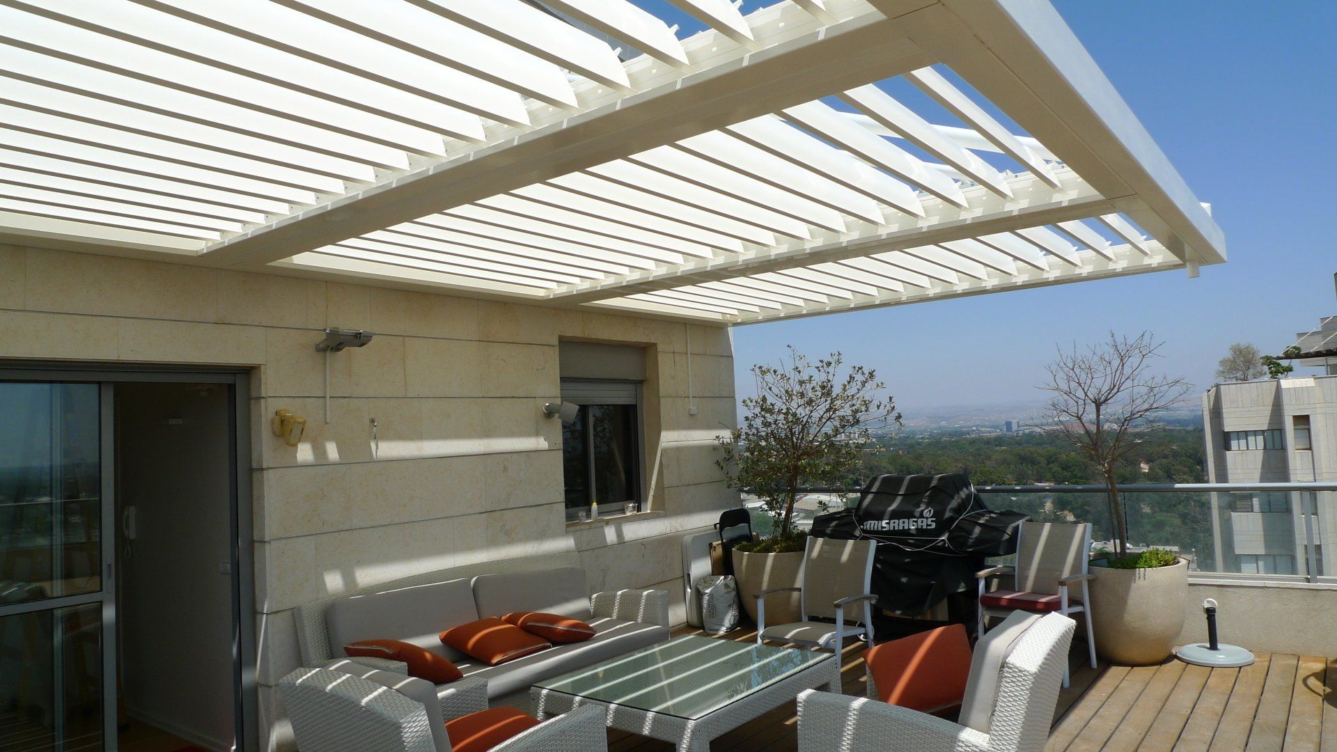 Sunlit rooftop patio with white pergola, patio furniture, and city view
