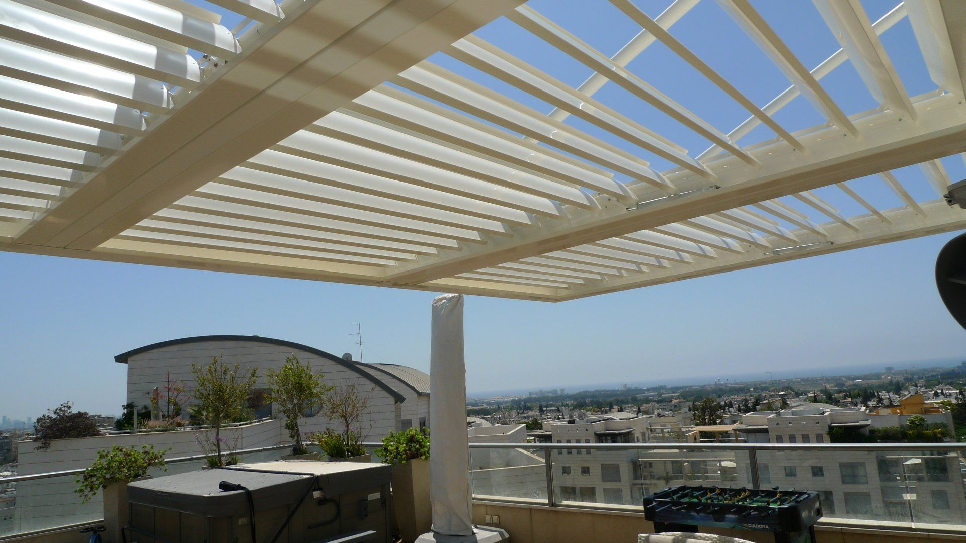 Rooftop terrace with white pergola, city skyline, and distant hills under a clear blue sky