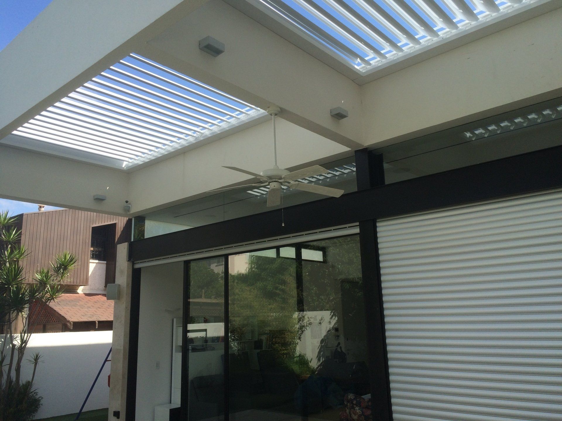 Modern patio with glass sliding doors and retractable roof shades beside a building