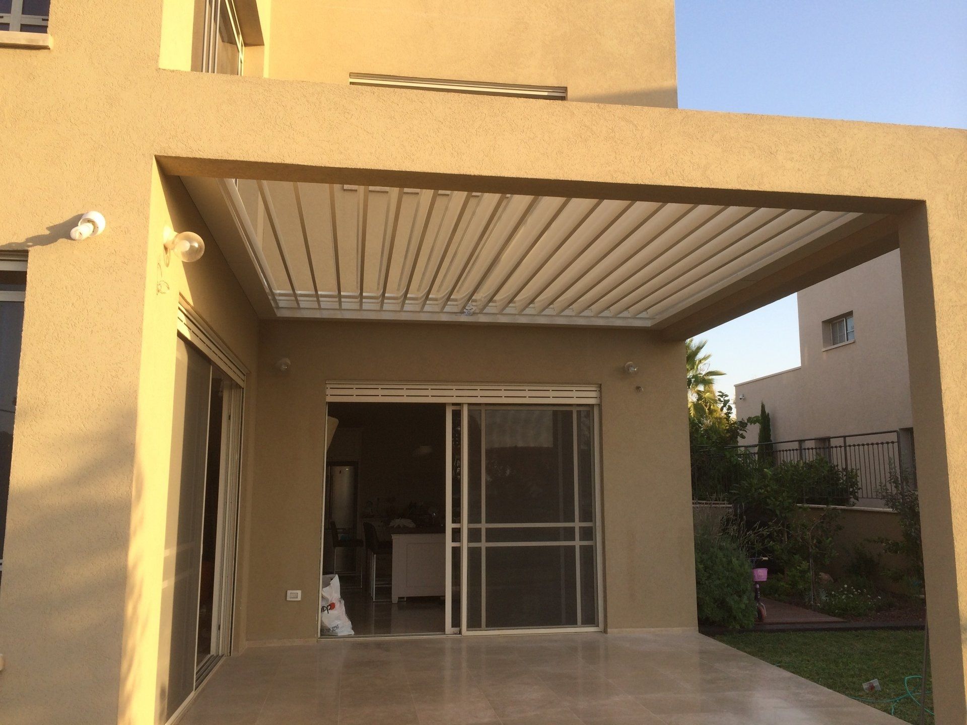 Covered patio with a sliding glass door and small lawn beside a beige house.